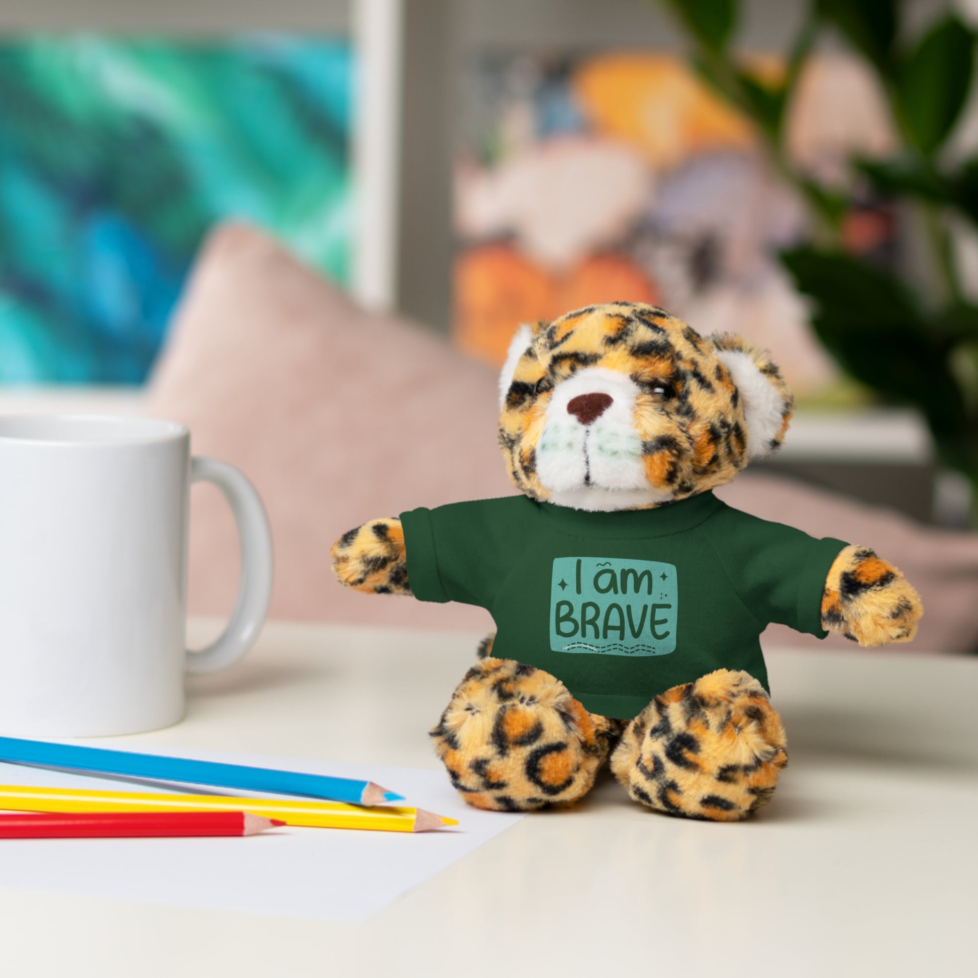 Cool Stuff Stuffies stuffed animal, wearing a removable I am Brave tee, displayed on a table. Part of a collection offering six customizable animal designs.