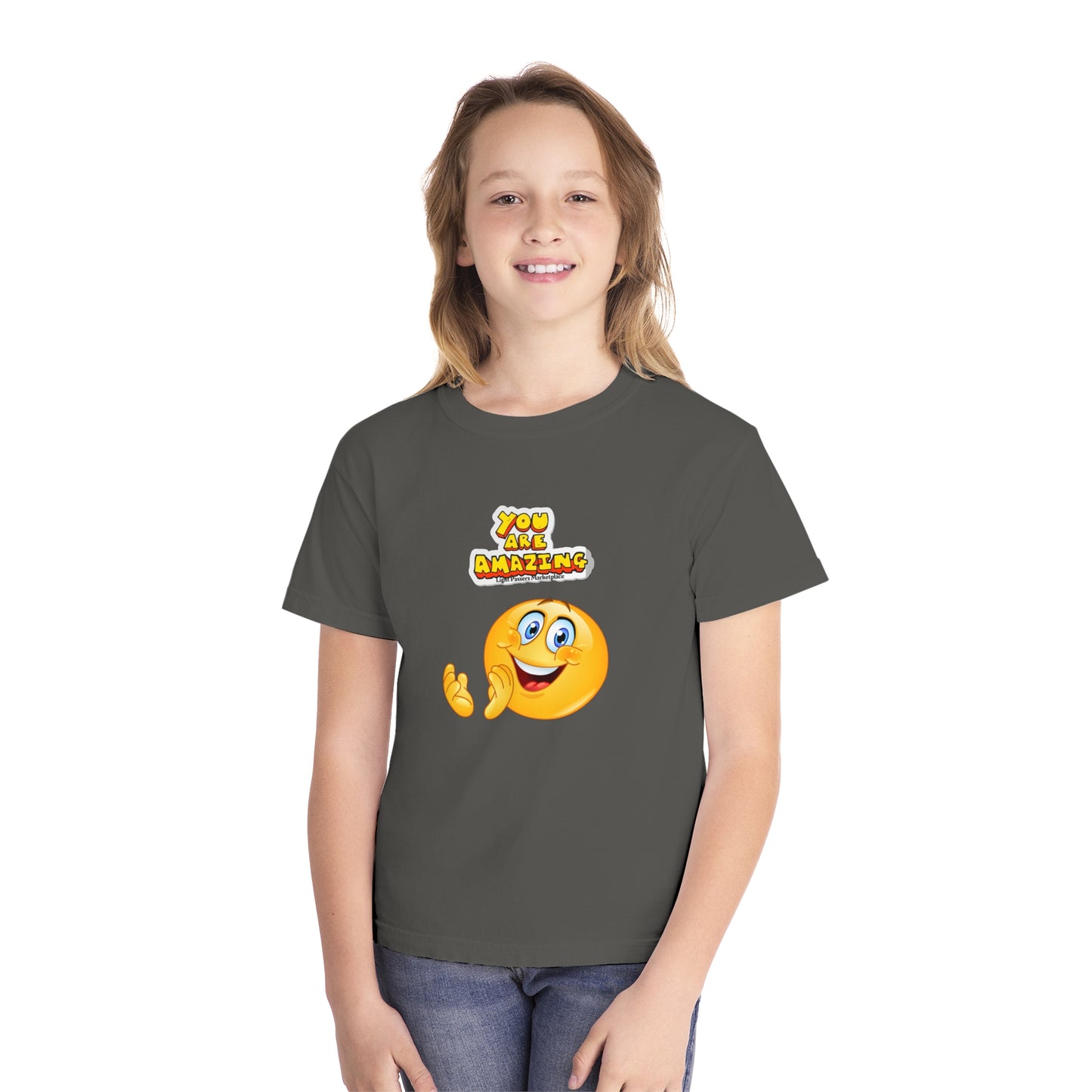 A girl in a grey tee with a cartoon face, showcasing the You are Amazing Clap Youth T-shirt. Made of soft-washed cotton for comfort and agility, perfect for active kids.