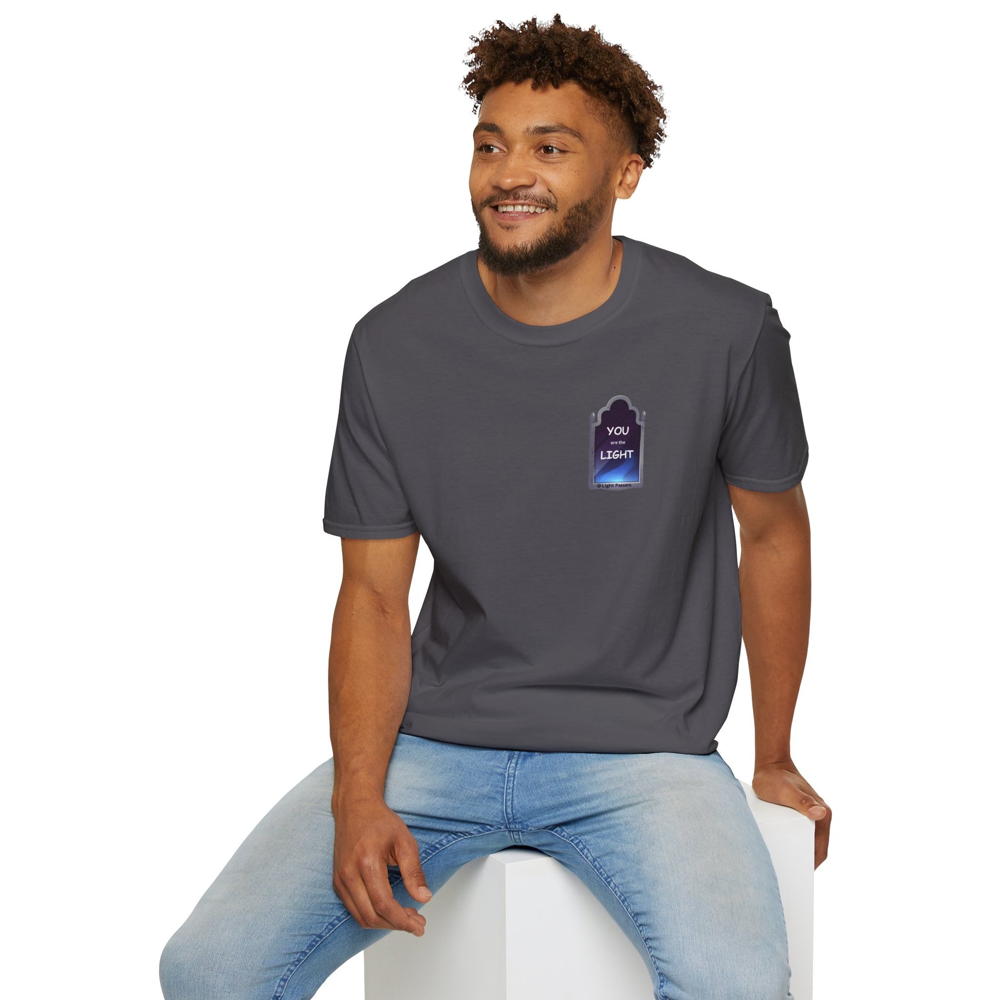 A man in a grey shirt sits on a cube, smiling with curly hair and a beard. Unisex heavy cotton tee, tear-away label, no side seams, for premium printing.