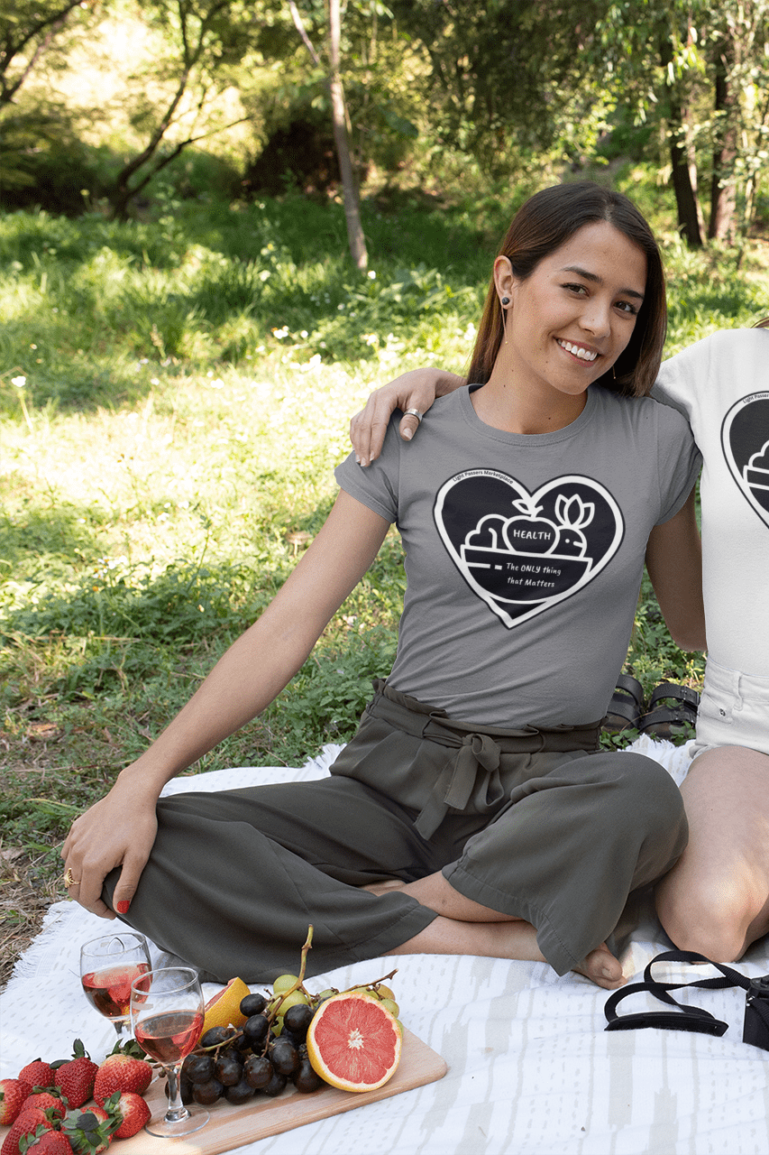 A group of women enjoying a picnic in the woods, one wearing a white shirt with a heart design, holding a glass of wine. The image features a picnic basket, wine glasses, and a camera.