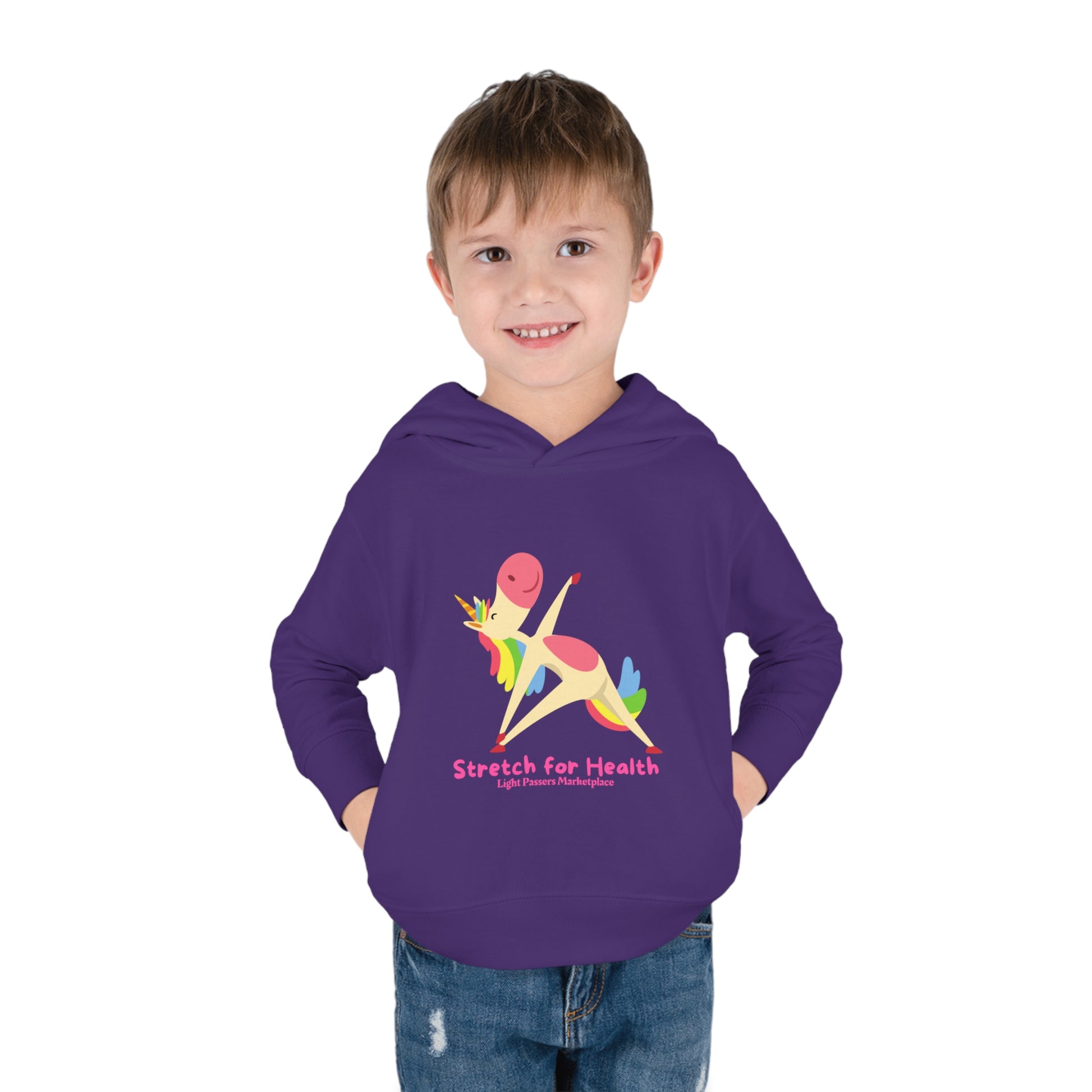 A smiling toddler in a Rabbit Skins Unicorn Stretch Toddler Hooded Sweatshirt with side seam pockets, jersey-lined hood, and durable stitching for lasting coziness.