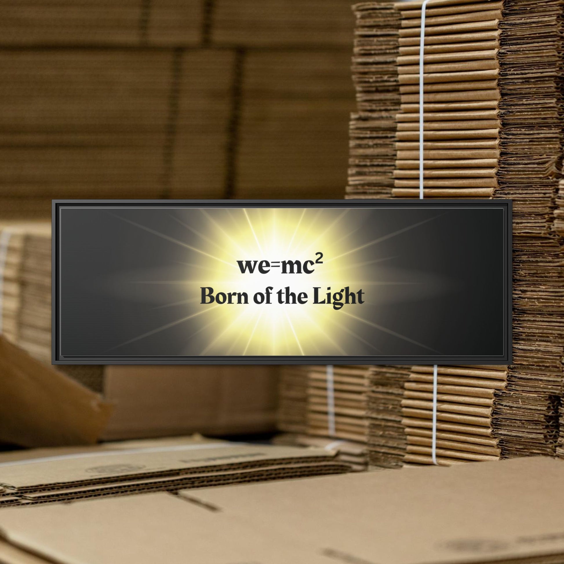 Inspirational Framed Canvas Art - we=mc² Born of the Light, featuring motivational text on a black frame, stacked on cardboard boxes. Ideal for uplifting home or office spaces.