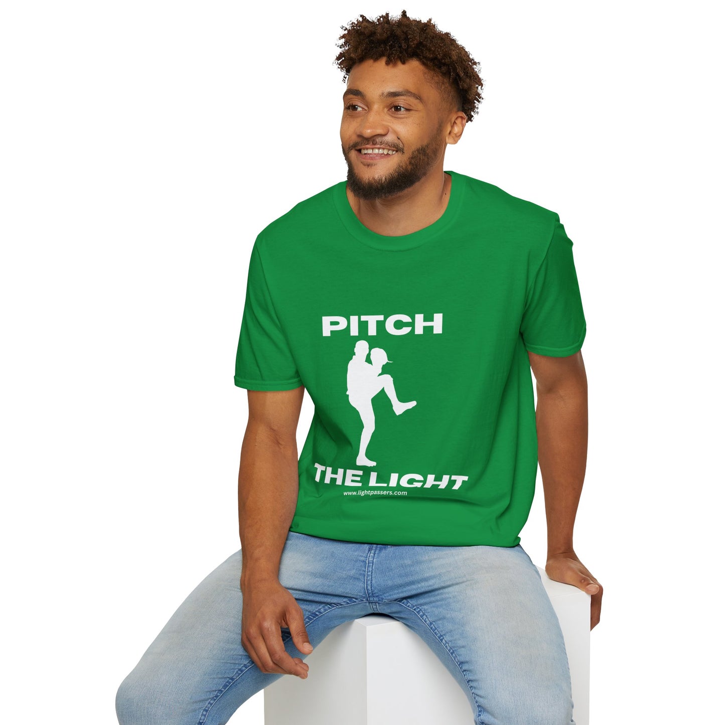 A man in a green shirt sits on a cube, showcasing the PITCH The LIGHT white lettering Unisex T-Shirt. The tee features soft 100% cotton, twill tape shoulders, and a ribbed collar for durability and comfort.