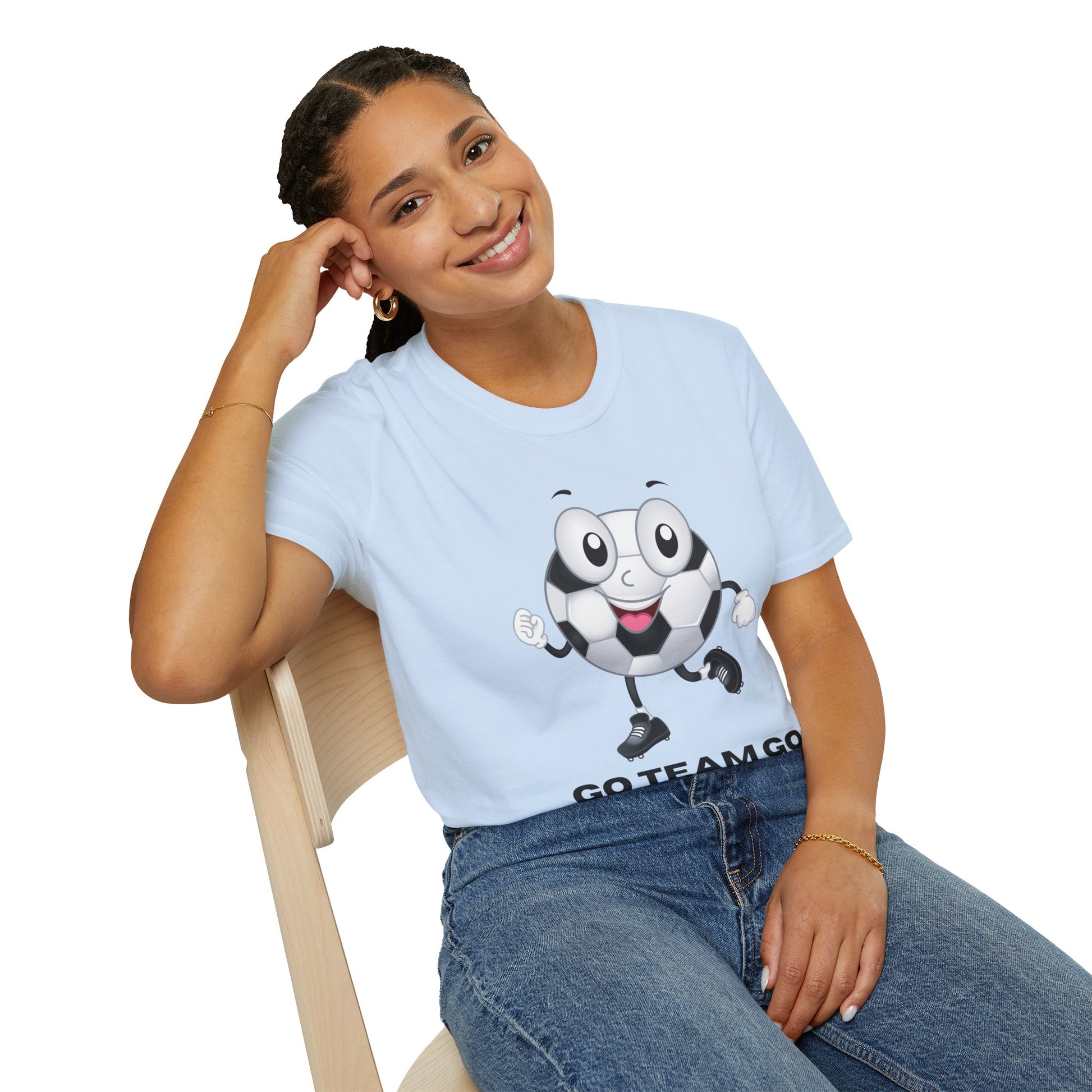 A woman in a white shirt with a cartoon football ball sits on a chair, smiling. The Soccer Ball Guy Team Unisex T-Shirt, 100% cotton, features a football ball design on the front.