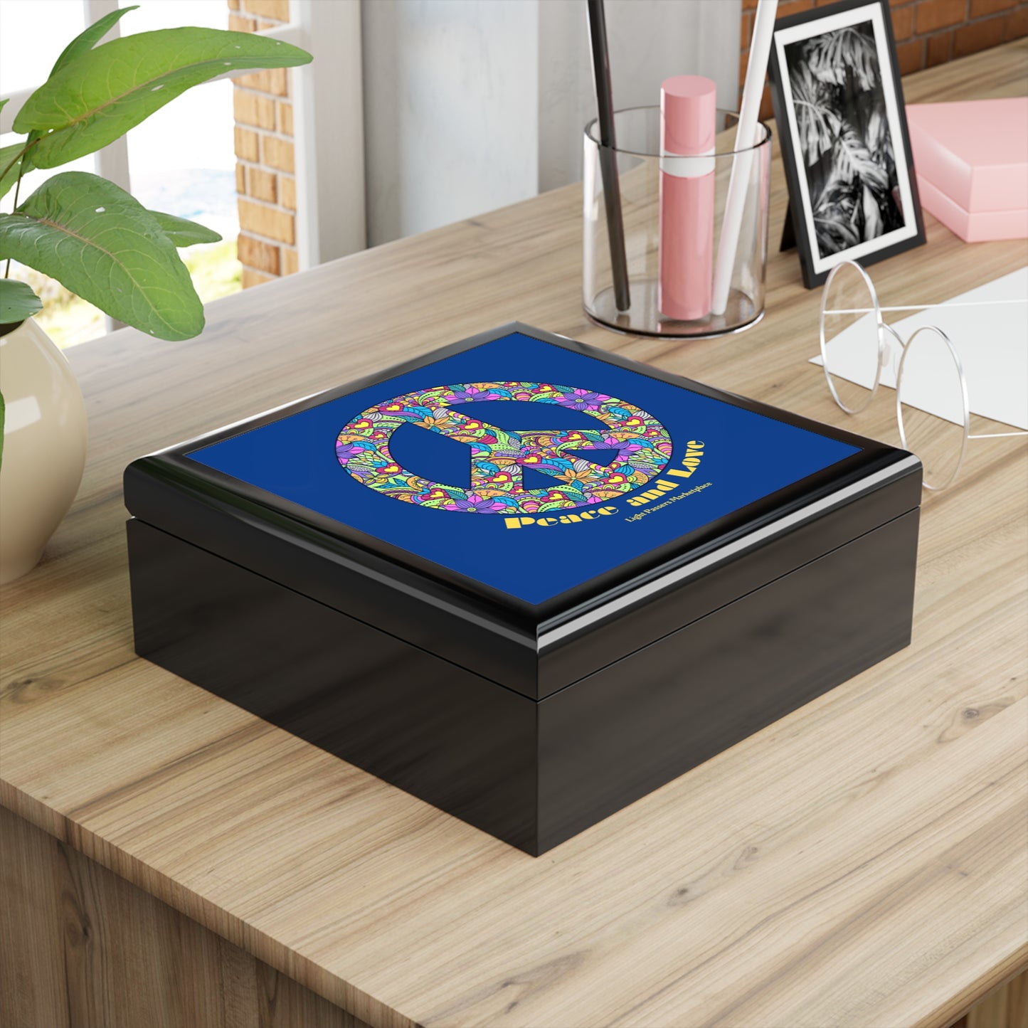 Flowered Peace Sign Wooden Jewelry Box on a desk, featuring a floral peace symbol lid, surrounded by a plant, pens, glasses, and a photo.