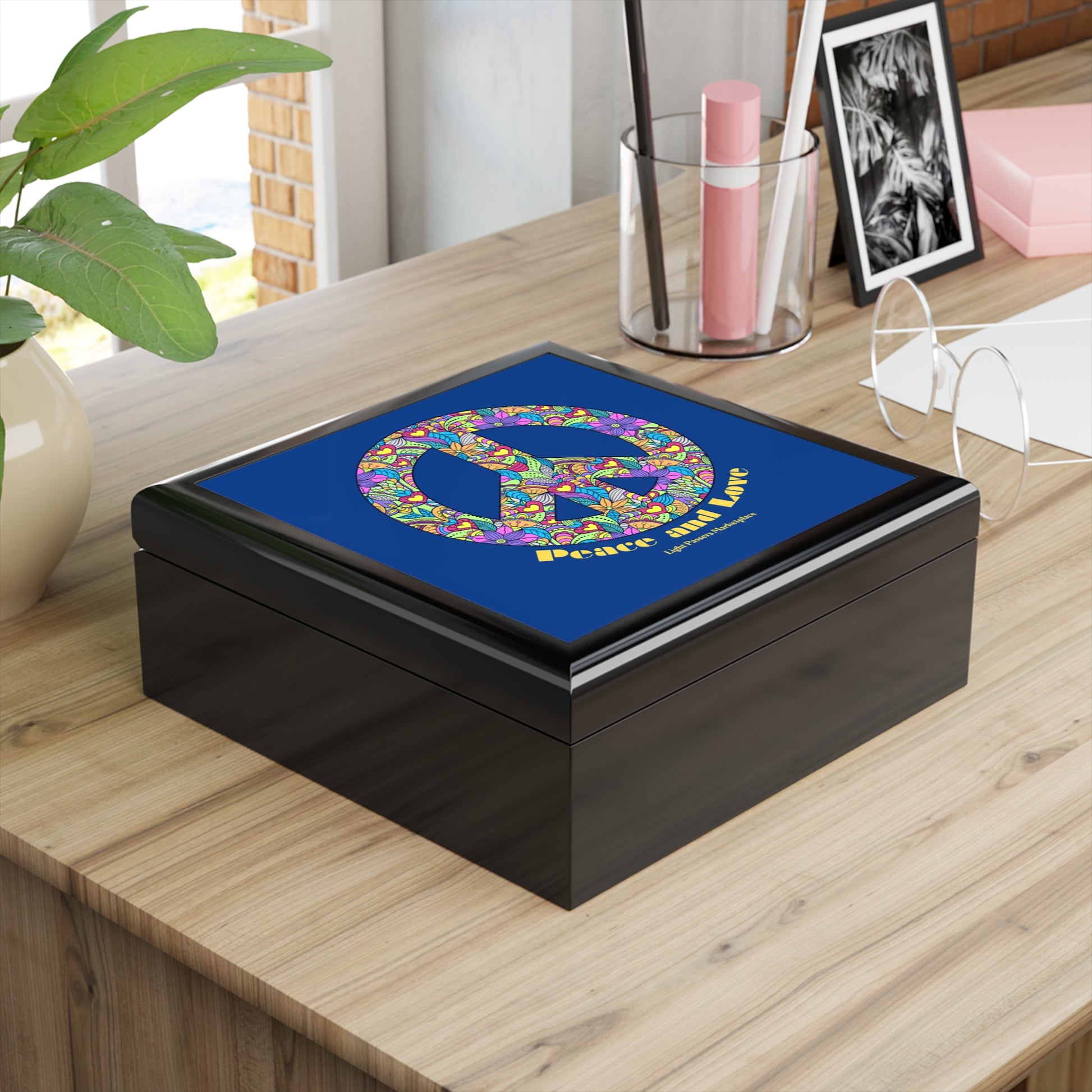 Flowered Peace Sign Wooden Jewelry Box on a desk, featuring a floral peace symbol lid, surrounded by a plant, pens, glasses, and a photo.