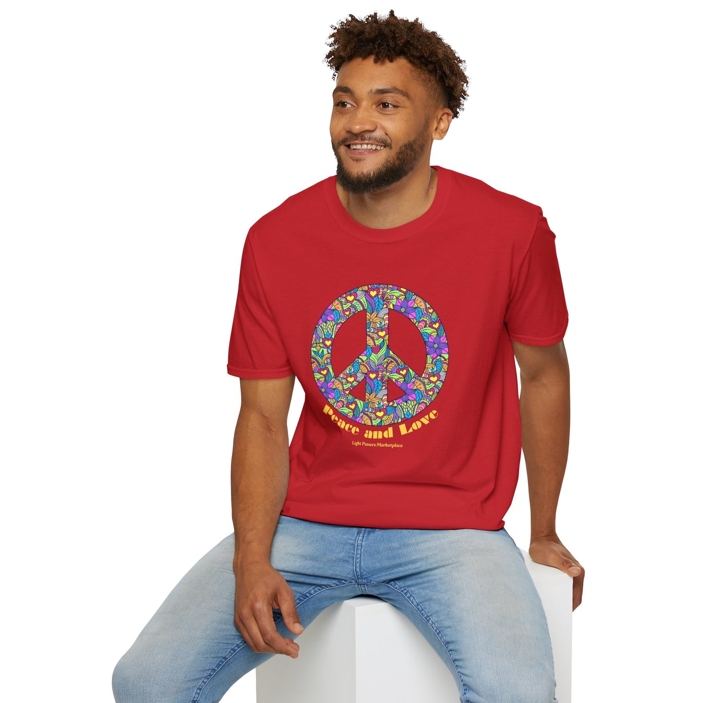 A man sits on a cube, wearing a red Peace sign with flowers Unisex T-shirt. The tee is 100% cotton, featuring twill tape shoulders for durability and a ribbed collar.