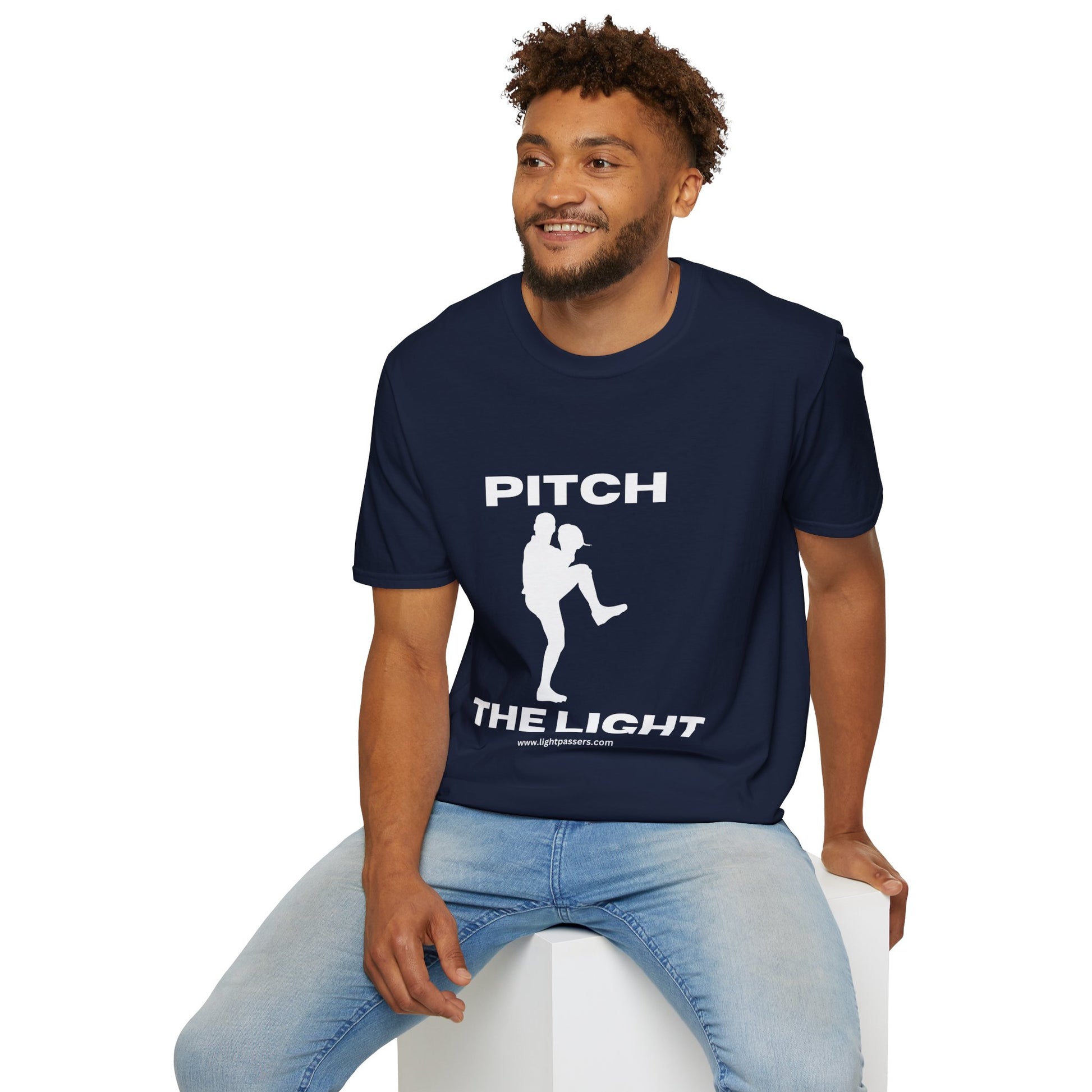 A man in a blue shirt sits on a cube, showcasing the PITCH The LIGHT white lettering Unisex T-Shirt. The tee features soft 100% cotton material, twill tape shoulders, and a ribbed collar.