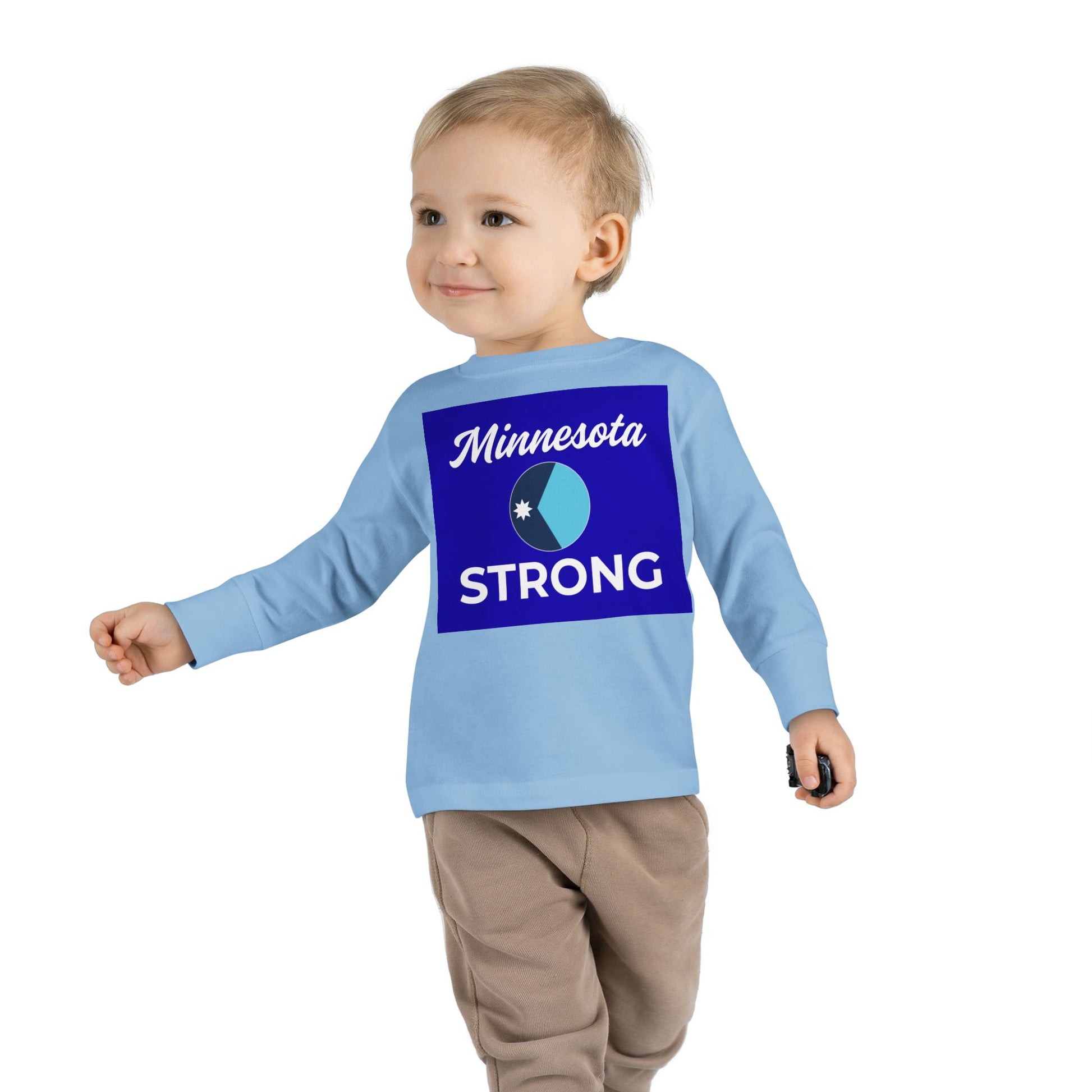Toddler wearing the Love and Peace The Light Minnesota Strong tee, showcasing community pride with a circular logo and holding a small toy.