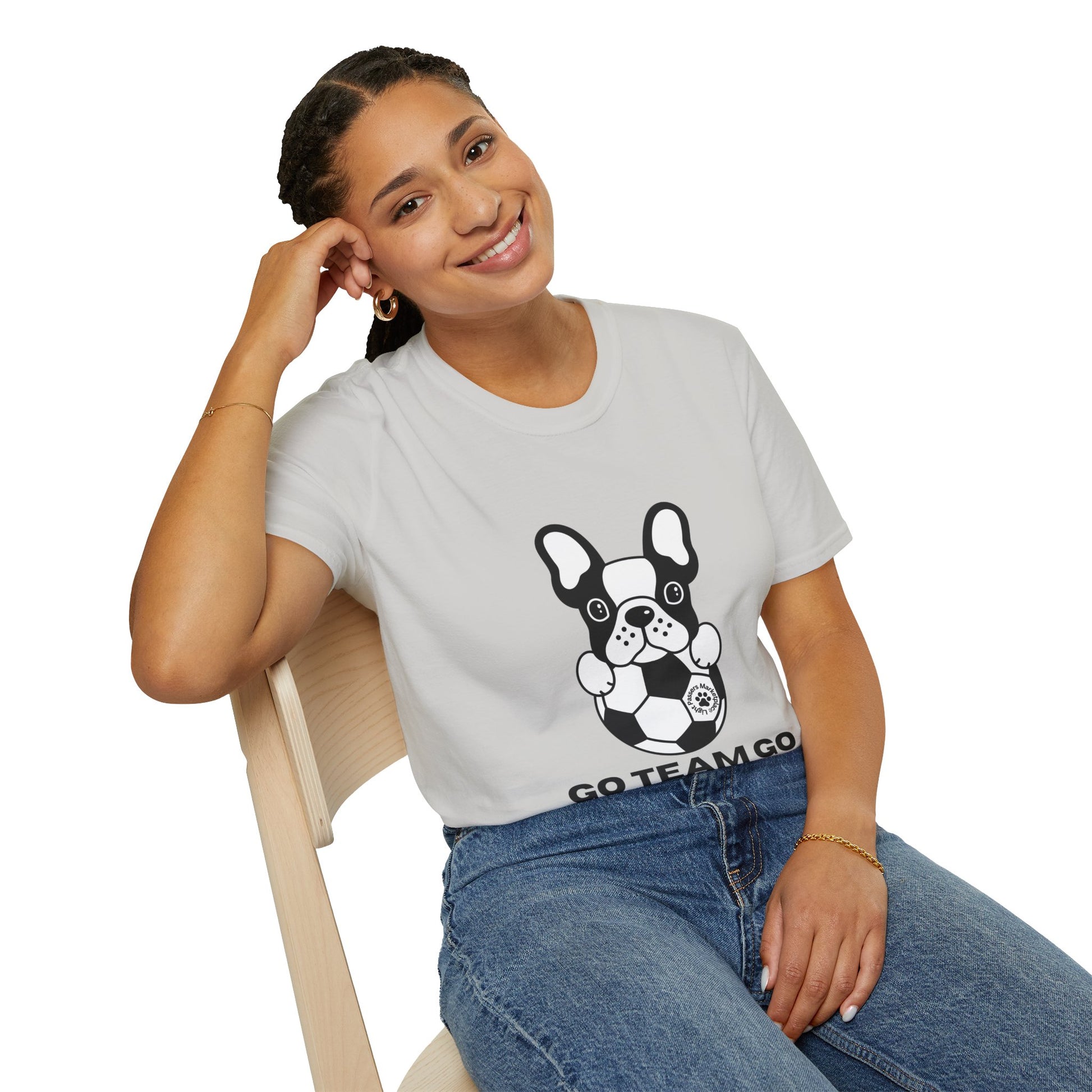 A woman in a white shirt with a dog on it smiles, sitting on a chair, showcasing the Soccer Dog Unisex T-Shirt's casual comfort and 100% cotton material with twill tape shoulders for durability.