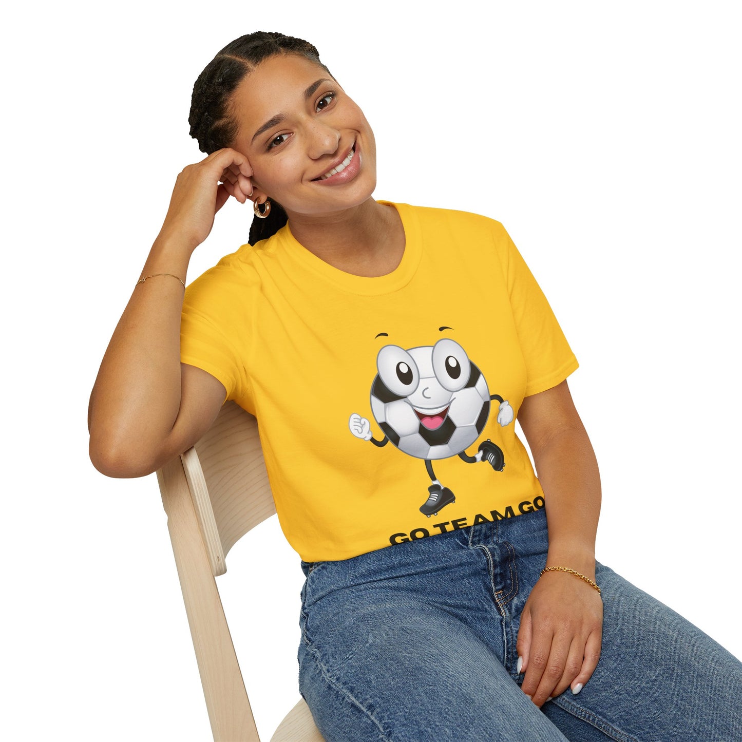 A woman in a yellow shirt and blue jeans sits on a chair, smiling. The product is a Soccer Ball Guy Team Unisex T-Shirt, made of soft 100% cotton with twill tape shoulders for durability and a ribbed collar.