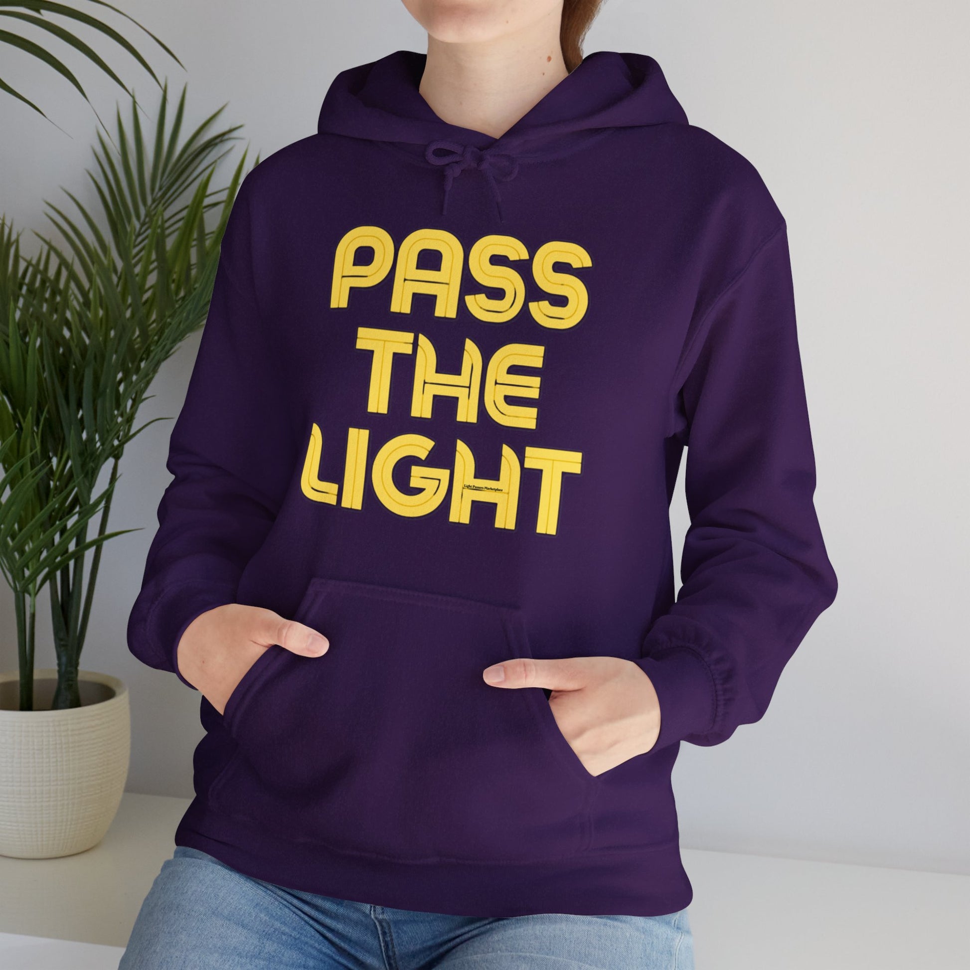 A person in a purple hoodie with yellow text, showcasing a cozy unisex heavy blend hooded sweatshirt. Features a kangaroo pocket and color-matched drawstring, made of 50% cotton and 50% polyester for warmth and comfort.