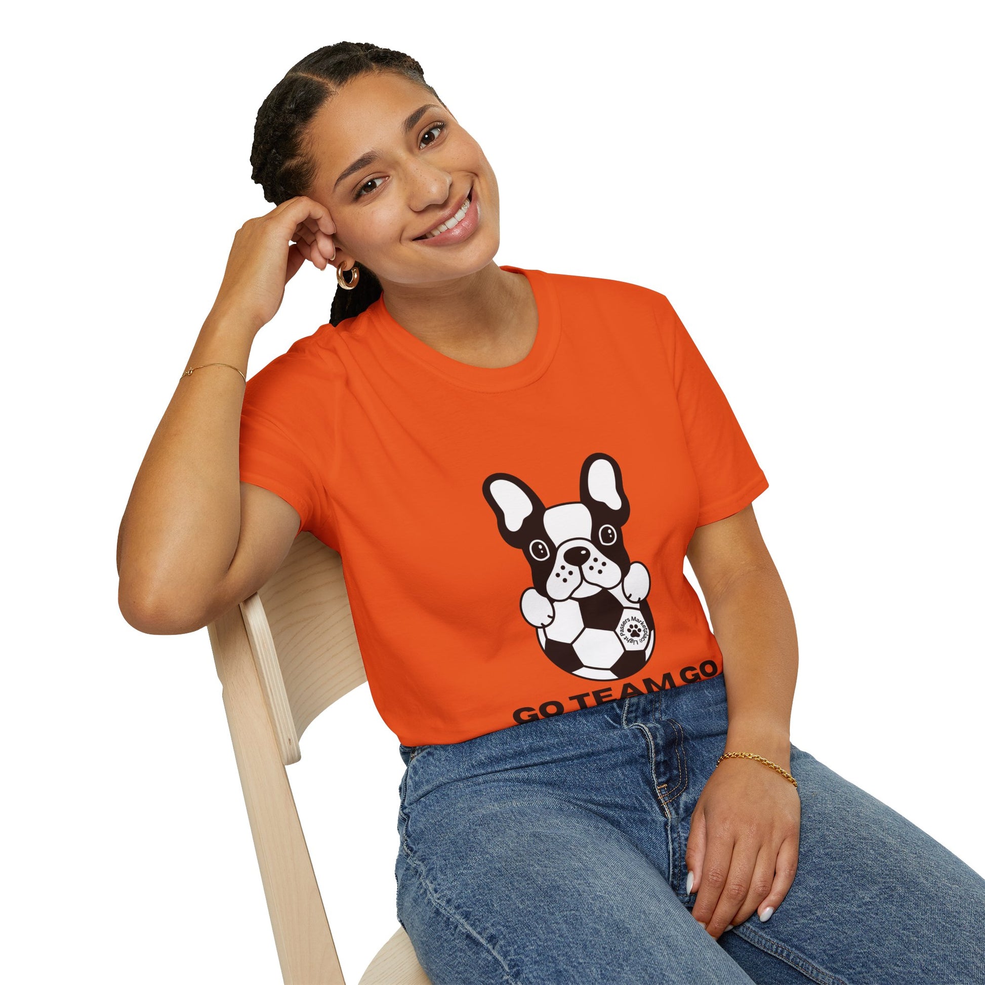 A woman in an orange shirt sits with a dog on her lap, showcasing the Soccer Dog Unisex T-Shirt. Soft 100% cotton tee with twill tape shoulders and ribbed collar for durability and comfort.