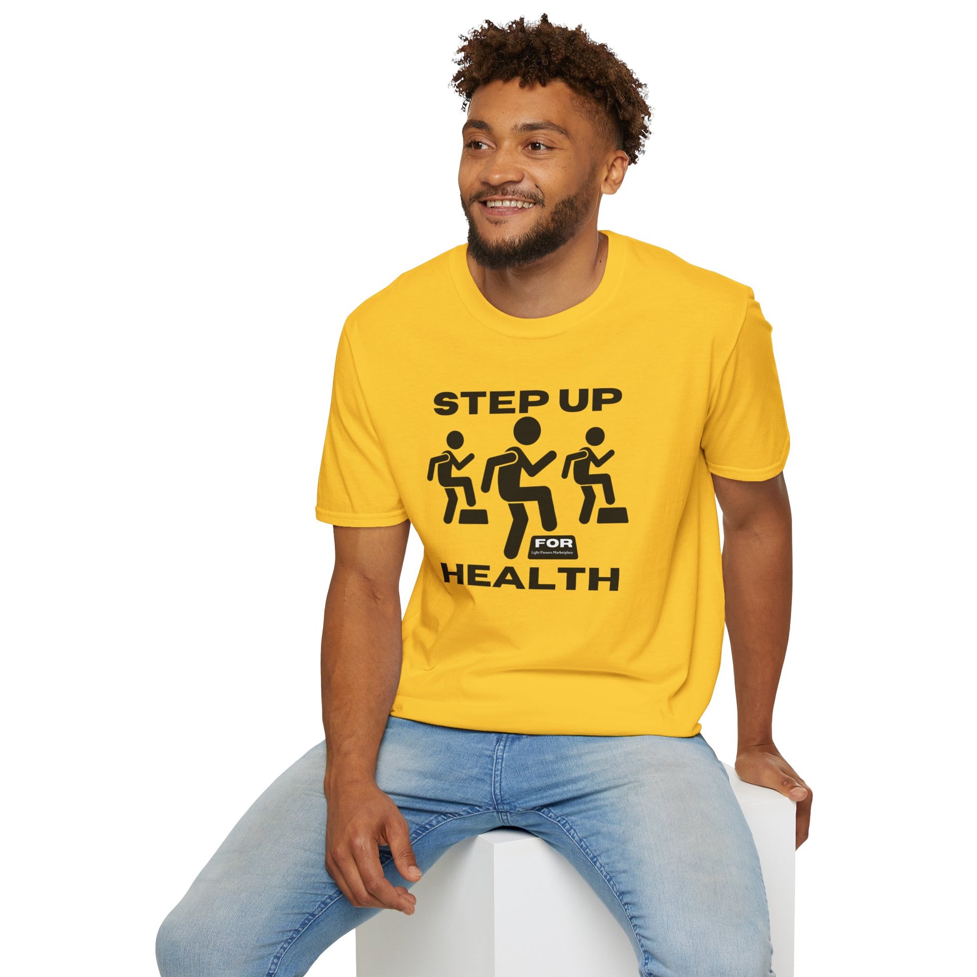 A man in a yellow Step Up For Health unisex t-shirt sits on a cube, showcasing the tee's soft 100% cotton fabric, twill tape shoulders, and ribbed collar for durability and comfort.