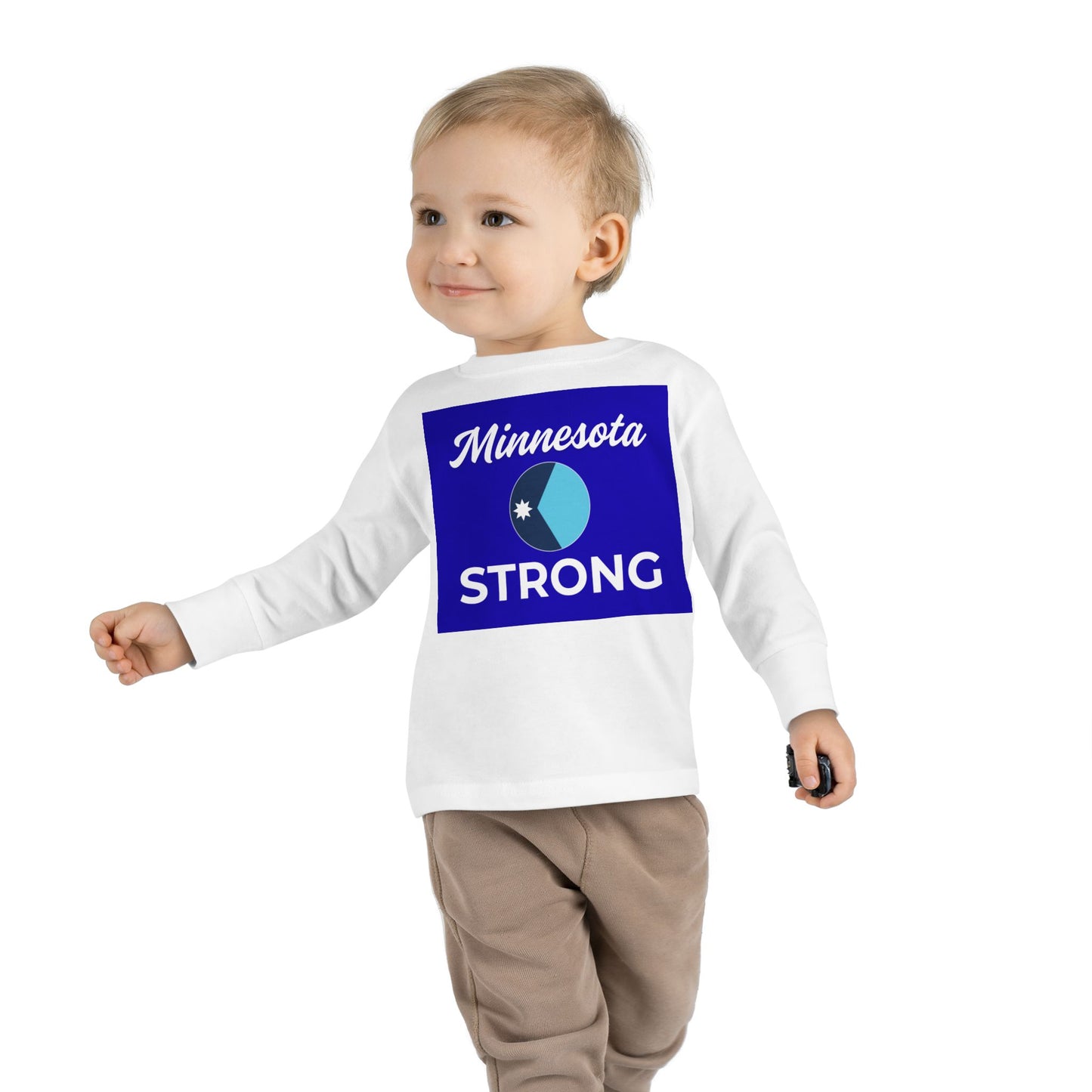 Toddler wearing Minnesota Strong long-sleeve tee from Light Passers Marketplace, featuring community pride graphic, paired with light brown pants, holding a toy car.