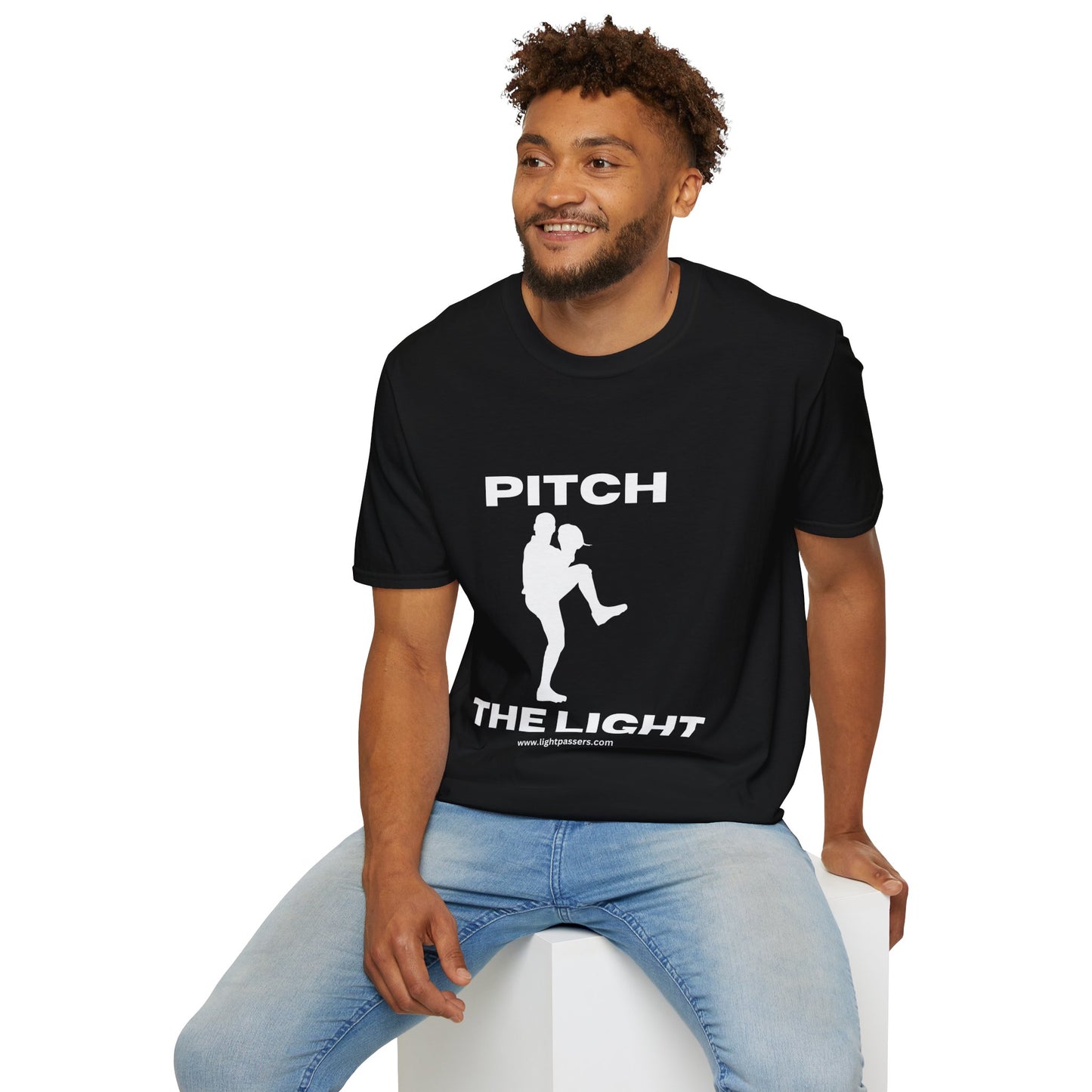 A man in a black shirt sits on a cube, showcasing the PITCH The LIGHT white lettering Unisex T-Shirt. The tee features soft 100% cotton, twill tape shoulders, and a ribbed collar for durability.