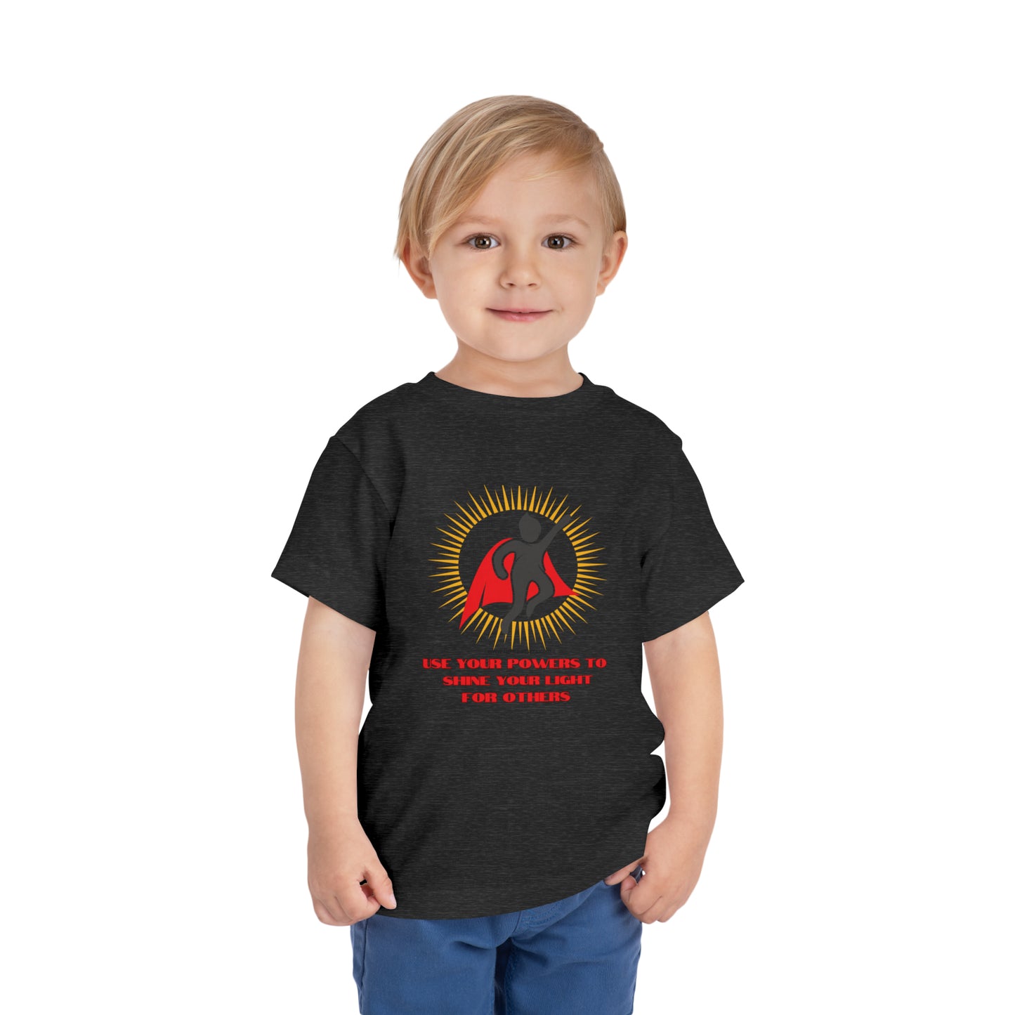 A toddler wearing a black Use Your Powers t-shirt, featuring a superhero logo. Made of 100% Airlume combed cotton for comfort. Tear-away label included.