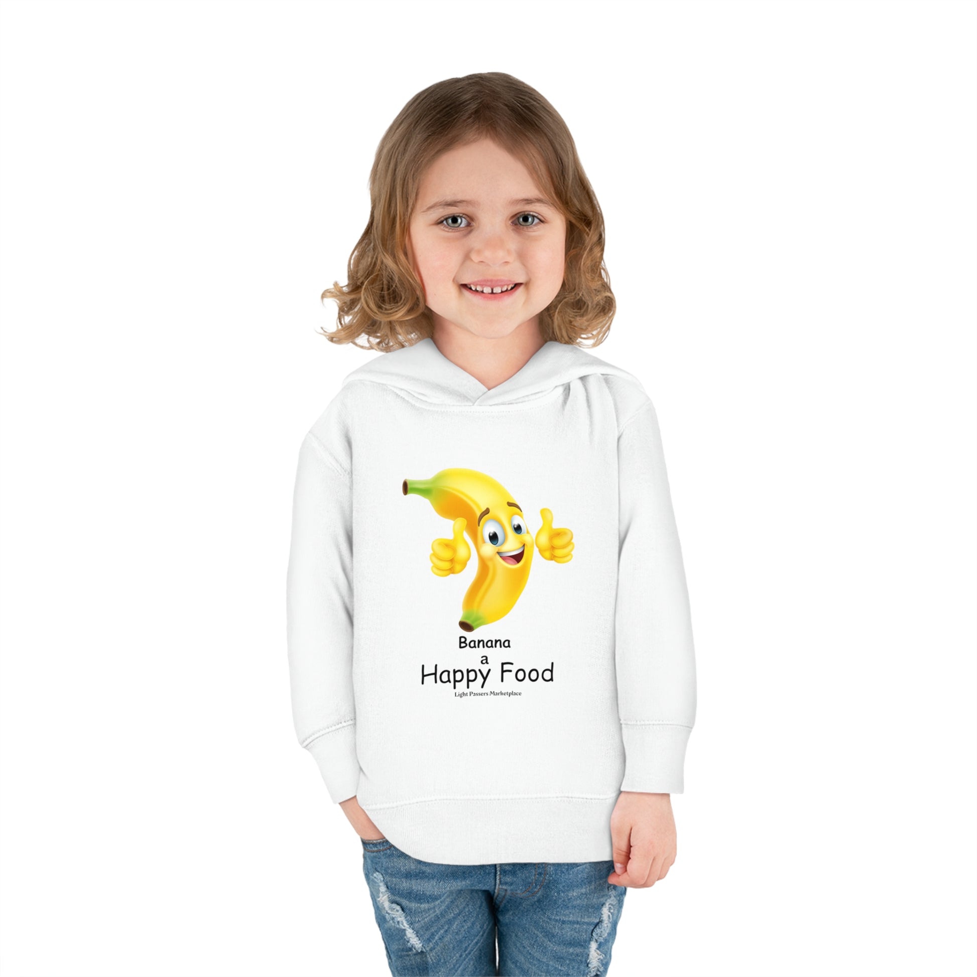 A toddler in a white Rabbit Skins hoodie with a cheerful banana design, smiling at the camera. Features jersey-lined hood, cover-stitched details, and side seam pockets for lasting coziness.