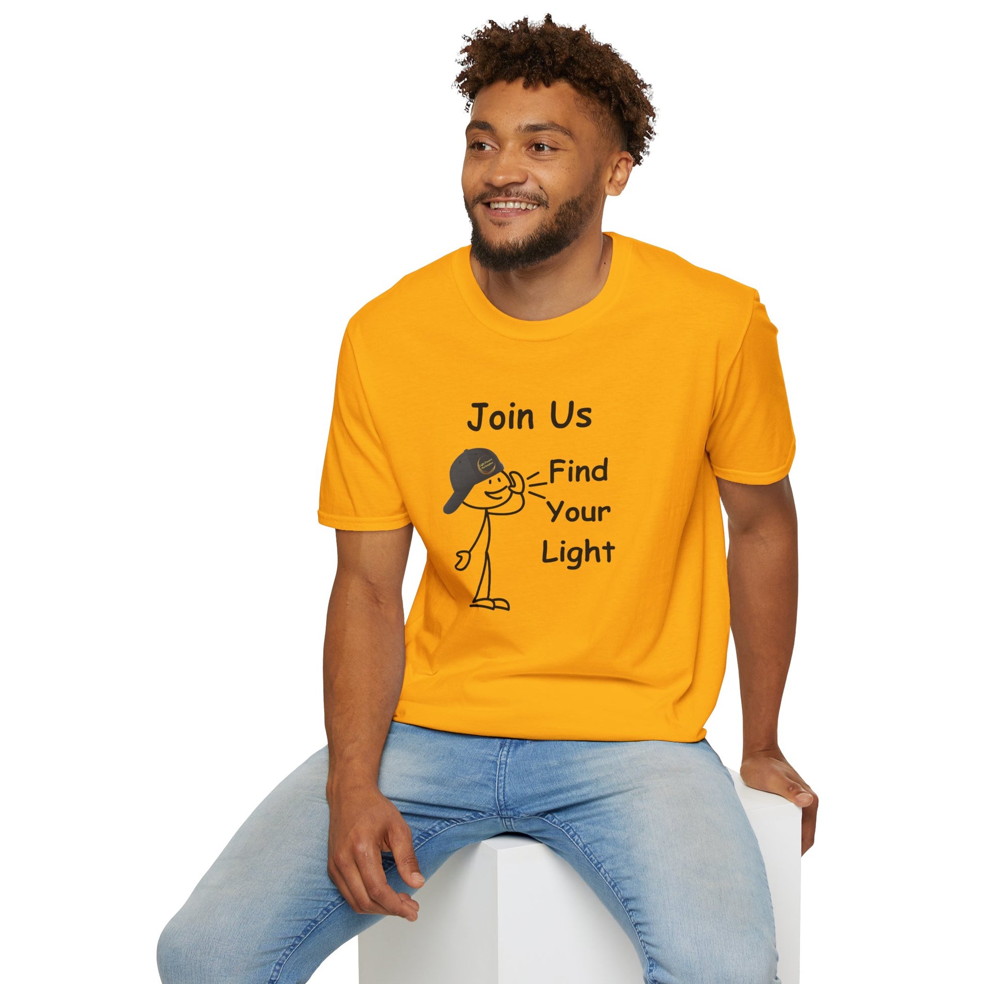 A man in a yellow shirt sits on a cube, showcasing the Join Us Find Your Light Unisex T-Shirt. Made of soft 100% cotton, featuring twill tape shoulders and a ribbed collar for durability and comfort.