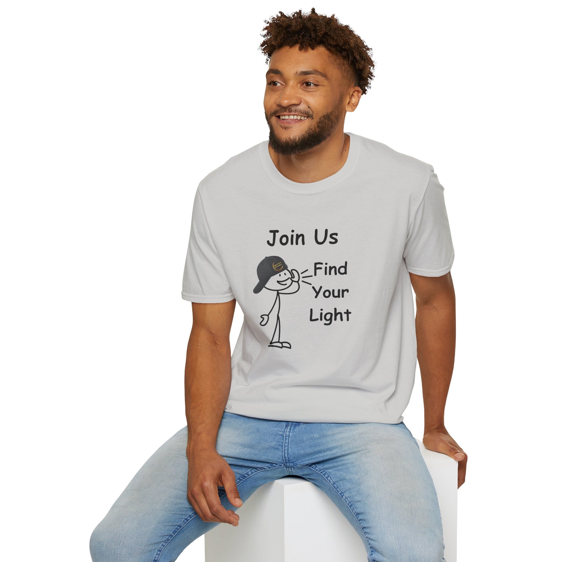 A man in a white shirt with a cartoon character sits on a cube, showcasing the Join Us Find Your Light Unisex T-Shirt. Made of soft 100% cotton, featuring twill tape shoulders for durability and a ribbed collar.