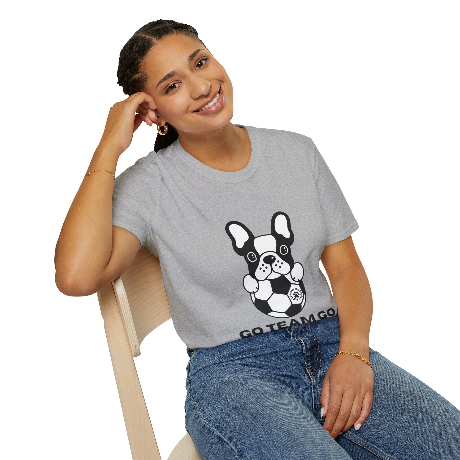 A woman in a grey shirt with a dog on it sits on a chair, smiling. A black and white dog with a football ball is also visible. The image is relevant for the Soccer Dog Unisex T-Shirt, a comfortable 100% cotton tee with twill tape shoulders and a ribbed collar.