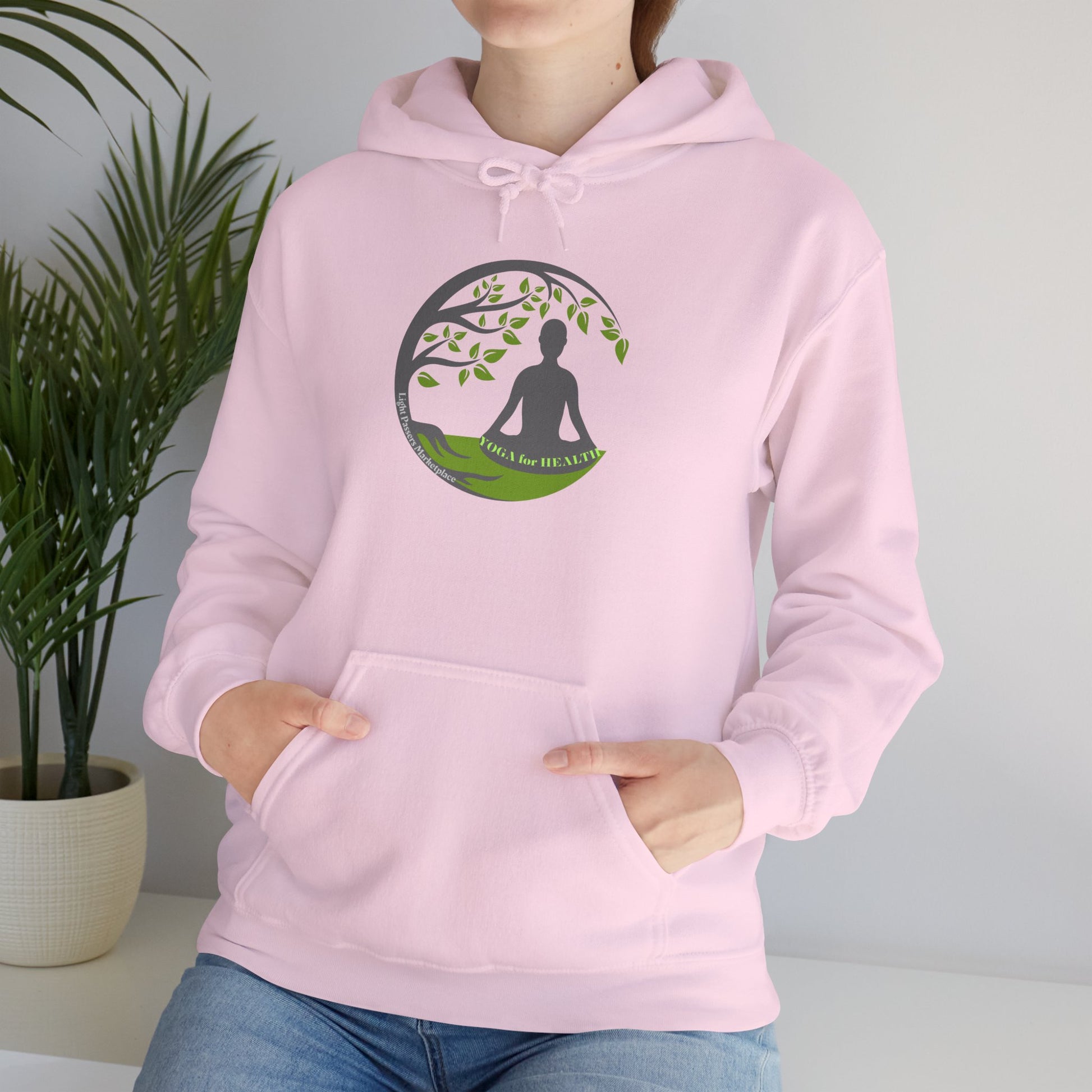 A woman in a pink hoodie meditates near a houseplant. Unisex heavy blend hooded sweatshirt with kangaroo pocket, drawstring hood, and cozy cotton-polyester fabric for warmth and comfort.