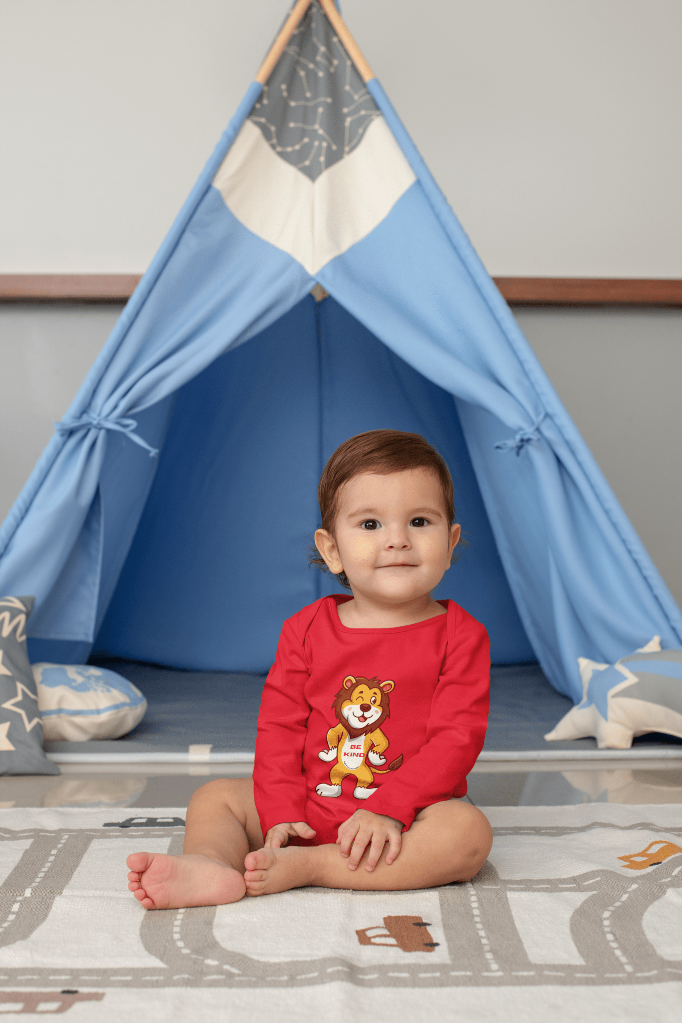 Baby wearing Be Kind Lion Baby Long Sleeve Onesie Bodysuit, sitting in a teepee, with a cartoon lion design visible.