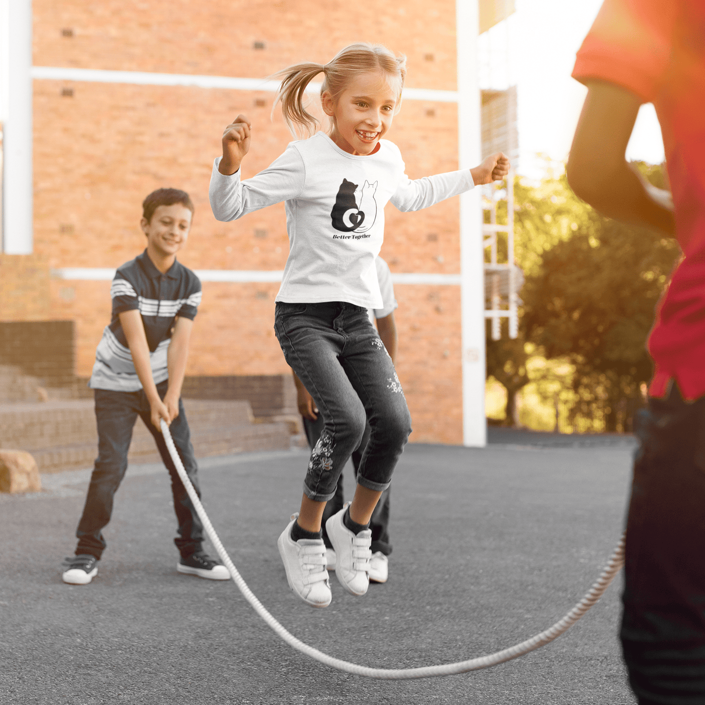 Youth Long Sleeve 2 Cats Heart Love Tails, showing kids playing outdoors. Features heart-shaped tail design of black and white cats, perfect for cat lovers.