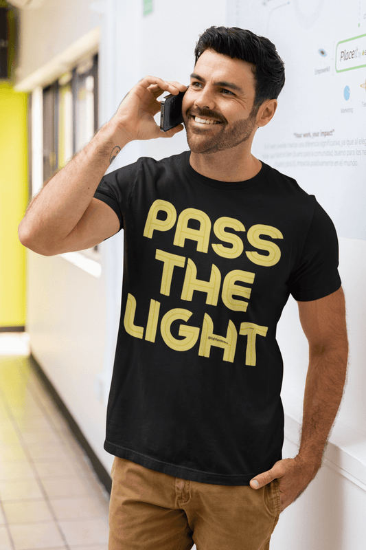 Man wearing The Light Pass The Light Adult Unisex T-shirt, featuring inspirational yellow text on black, talking on a cell phone. The tee offers a classic fit and durable design.