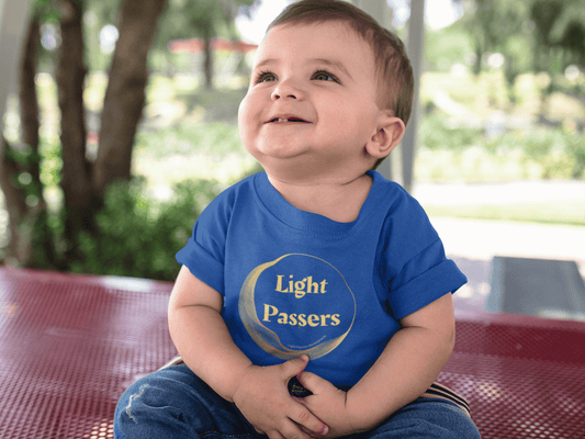 A baby sitting on a bench, wearing a Light Passers Logo Baby T-shirt. Infant fine jersey tee with side seams, ribbed knitting, and taped shoulders for comfort and durability.