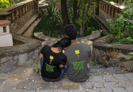 A man and woman sit on stone steps, showcasing the Beauty and the Light Unisex T-shirt BACK. Classic fit, 100% cotton tee with smooth surface for premium printing.