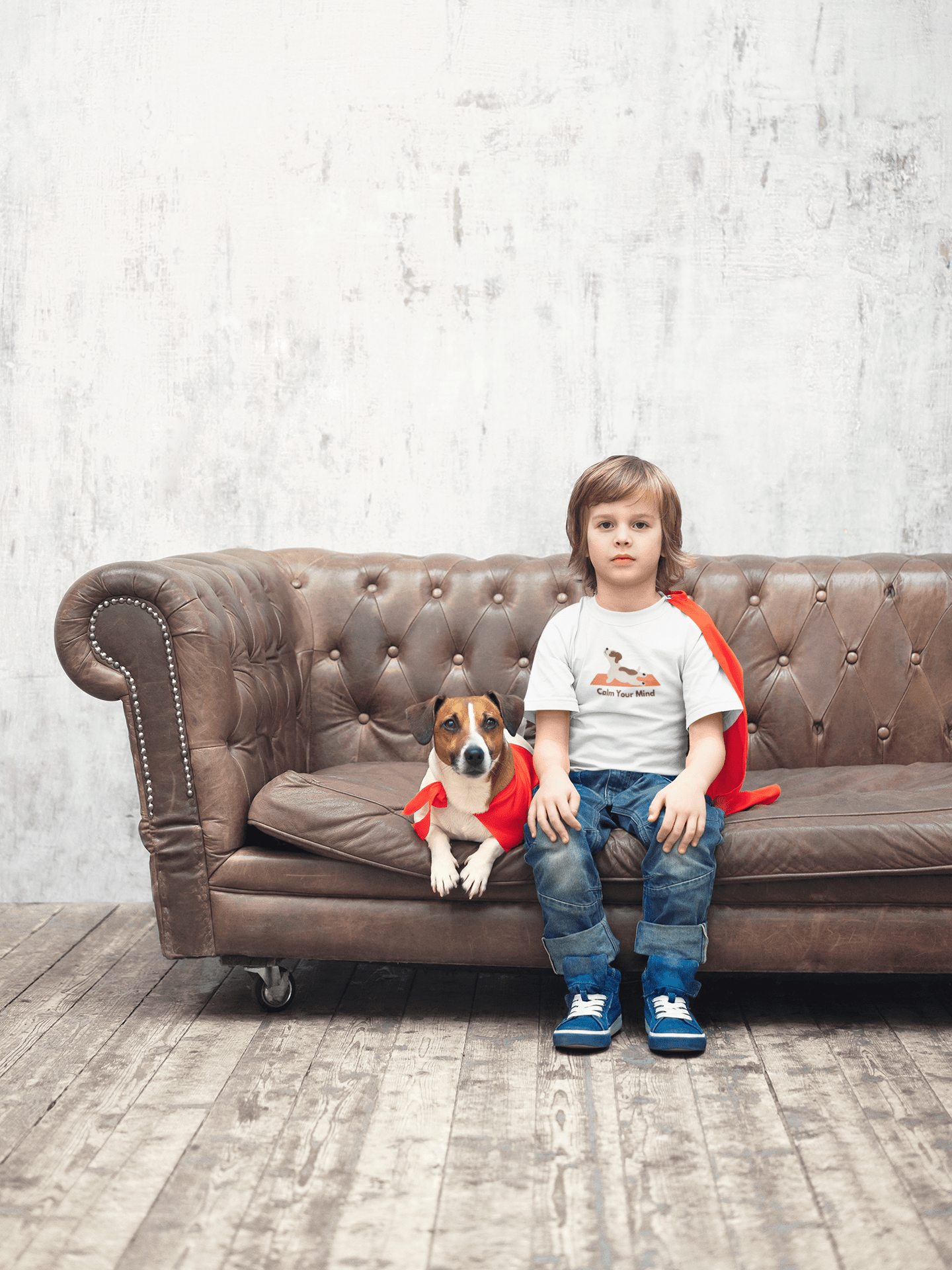 A toddler in a white tee sits on a couch with a dog, showcasing a red cape. Soft 100% combed cotton, tear-away label, classic fit.