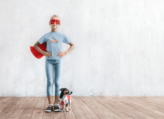 A girl in a superhero garment stands with a dog. Kids heavy cotton tee, 100% cotton, twill tape shoulders, curl-resistant collar, no side seams, ethically made, Oeko-Tex certified.