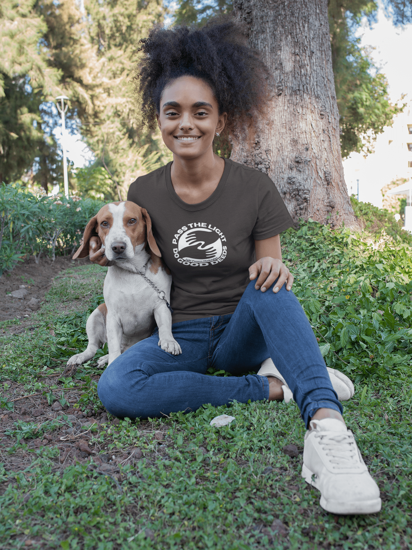 A woman sits on grass with a dog, showcasing the Pass the Light Do Good Deeds Unisex T-shirt. The heavy cotton tee offers a classic fit, smooth surface for vivid prints, and durable tape on shoulders.