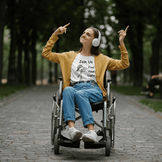 A woman in a wheelchair points at something, wearing headphones, showcasing the Join Us Find Your Light Unisex T-Shirt. Unisex tee made of soft 100% cotton, featuring twill tape shoulders for durability.