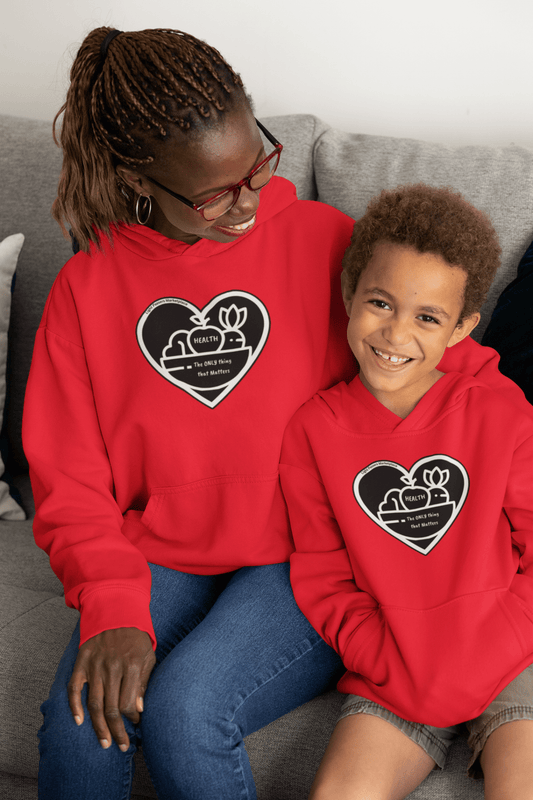 A woman and a boy in matching red sweatshirts sit on a couch. Fruit Basket Toddler Hoodie with jersey-lined hood and side seam pockets for cozy durability.