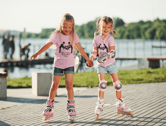 Two girls in roller skates holding hands, one wearing a pink shirt and knee pads. Kids heavy cotton tee, 100% cotton, twill tape shoulders, ribbed collar. Life is a Puzzle Work with a Team Youth T-shirt.