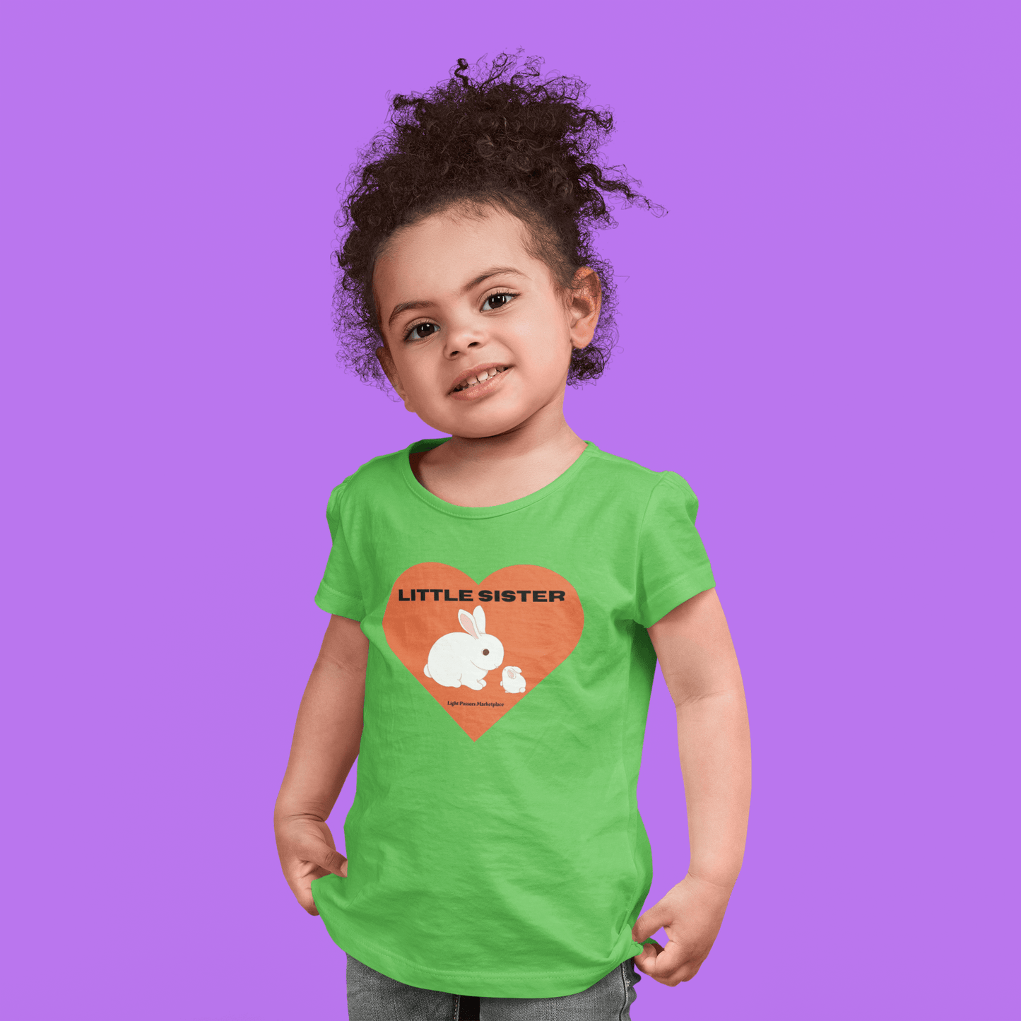 A young girl in a green shirt, close-up of a toddler's chest, wearing a Little Sister Toddler T-shirt. Soft, 100% combed cotton, durable print, tear-away label, classic fit.