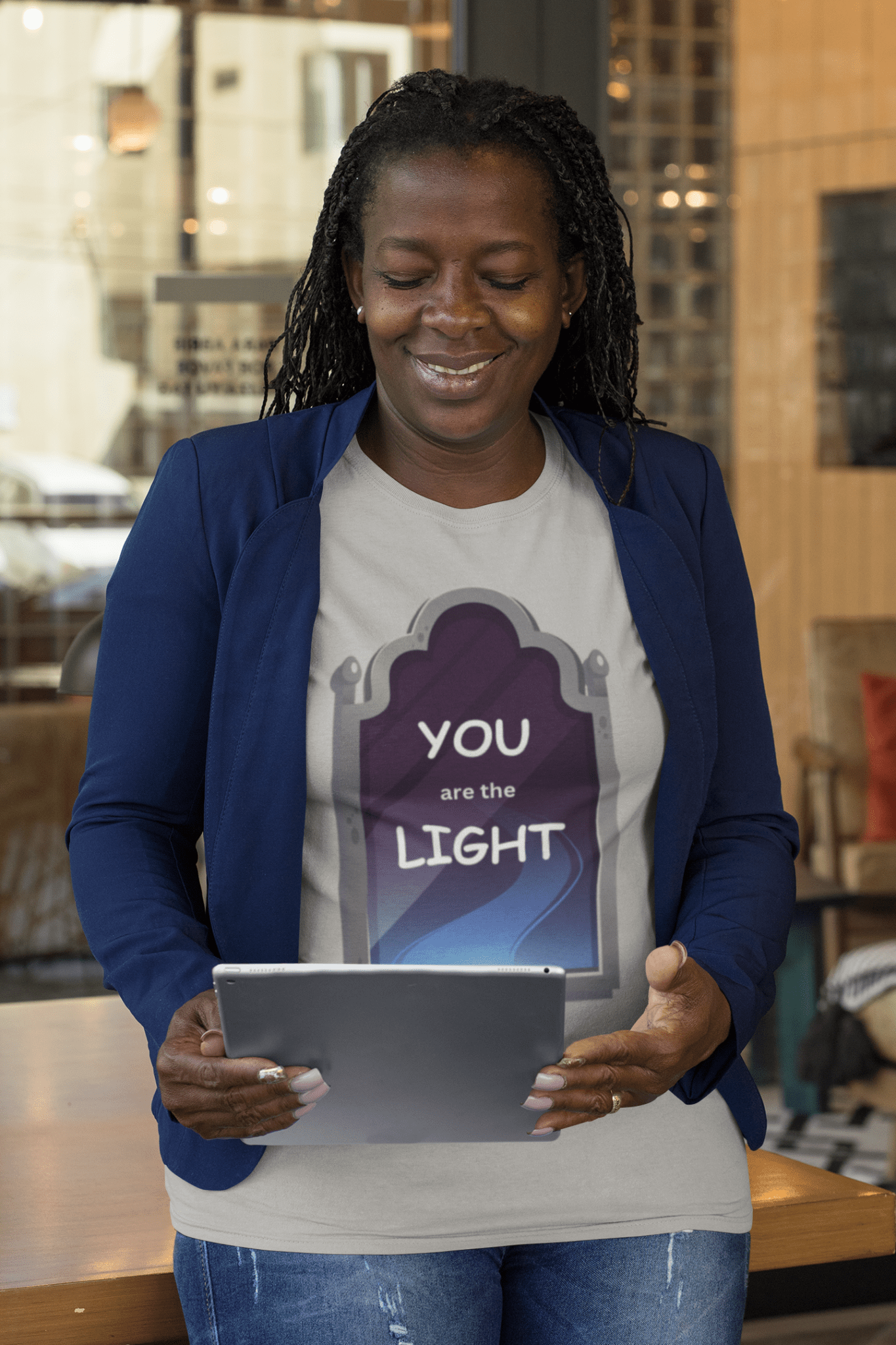 A woman with braided hair smiles, holding a tablet, showcasing the Light Mirror Unisex T-shirt. Classic fit, 100% cotton tee for premium printing quality.