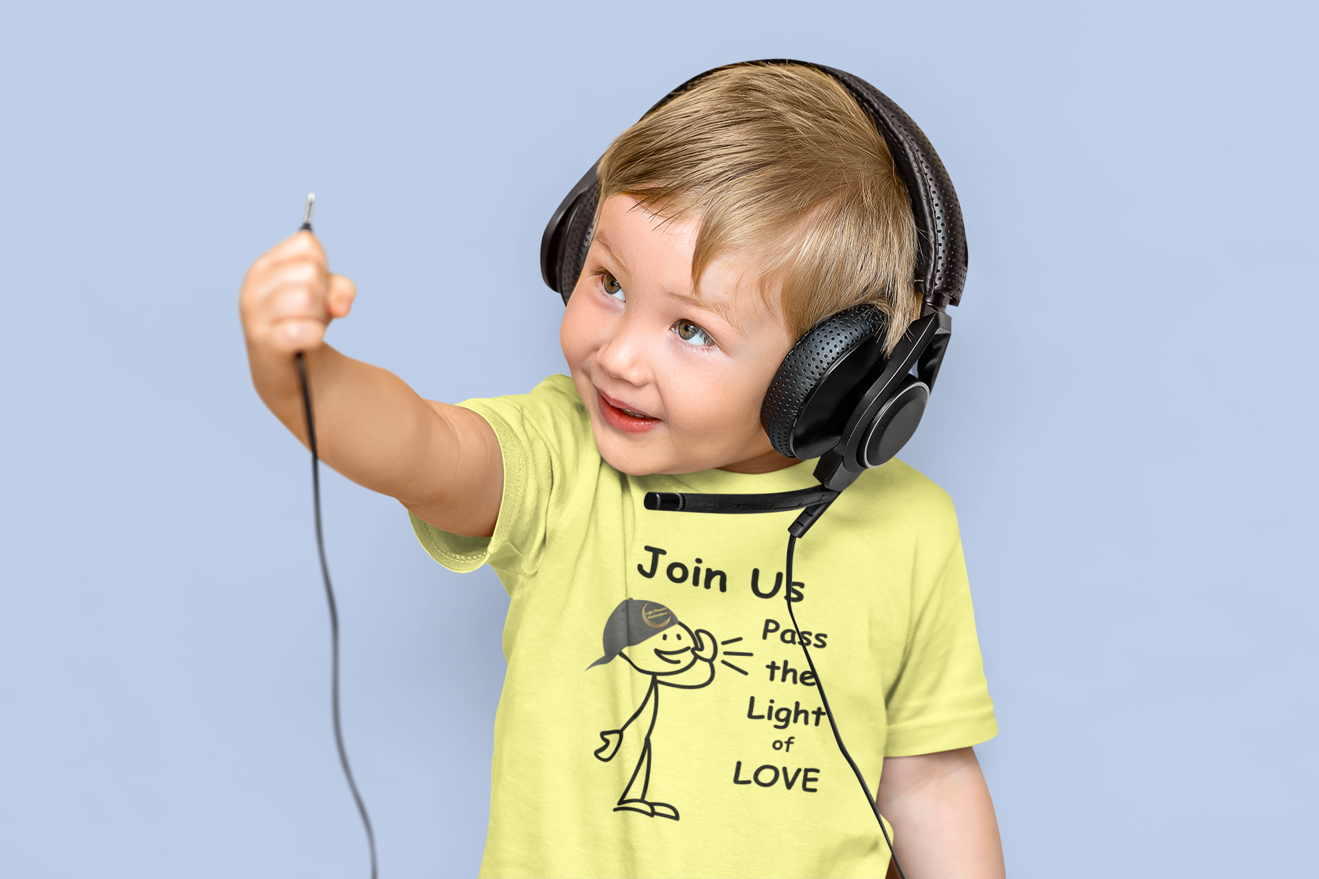 A child in a yellow shirt with a cartoon character, wearing headphones, holding a cord. Bella Canvas toddler t-shirt: 100% Airlume cotton, tear-away label, light fabric.