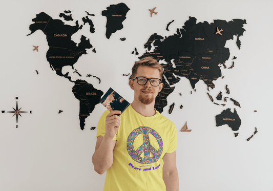 A man holding a passport in front of a world map, a peace sign with colorful flowers, and a hand holding a map. The Peace sign with flowers Unisex T-shirt, 100% ring-spun cotton, no side seams, ribbed collar, and tear-away label for comfort.