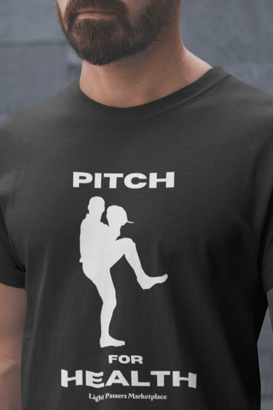 A man in a black shirt, showcasing the Pitch for Health Unisex T-Shirt. Made of soft 100% cotton, featuring twill tape shoulders for durability and a ribbed collar. Ethically crafted with US cotton.