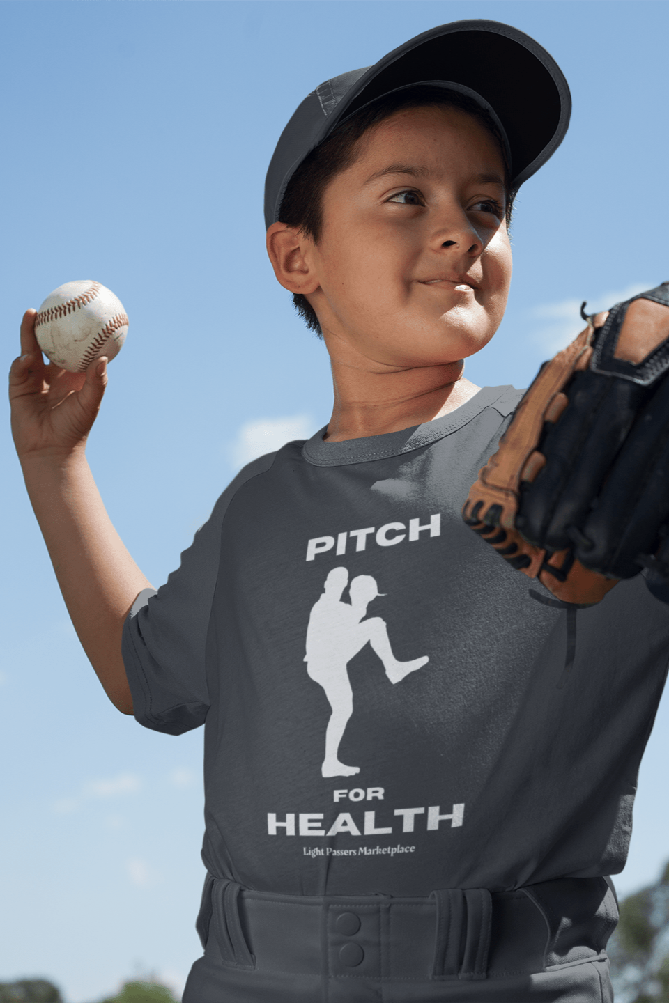 A boy holds a baseball and glove, wearing a hat, showcasing the Pitch for Health Youth Cotton T-shirt. Made of 100% cotton, featuring twill tape shoulders and ribbed collar for durability and comfort.