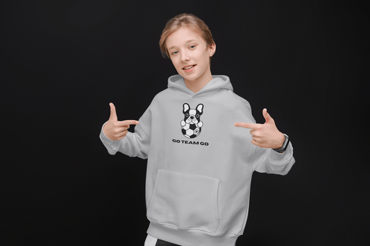 A boy points at Soccer Dog Youth Hooded Sweatshirt, featuring kangaroo pocket, twill taping, 50% cotton 50% polyester blend for printing, and ultra-soft fleece.
