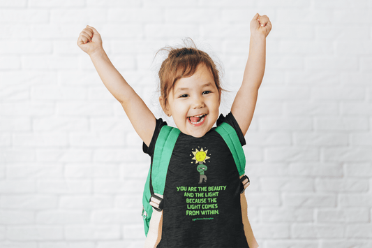 A toddler in a custom Bella Canvas tee, arms raised, with a backpack. Close-ups of a smiling face, mouth, and nose. Light bulb drawings add a playful touch.