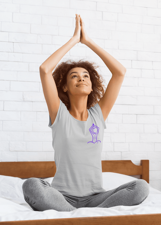 A woman in a grey shirt sits on a bed with her hands raised, embodying relaxation and comfort. Unisex Yoga Find Your Light small image T-Shirt, 100% cotton, soft fabric, tear-away label, Eurofit, no side seams.