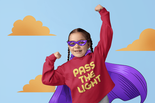 A girl in a superhero garment with a red shirt, purple cape, and glasses, showcasing Pass the Light Toddler Hooded Sweatshirt features like jersey-lined hood and side-seam pockets for cozy durability.