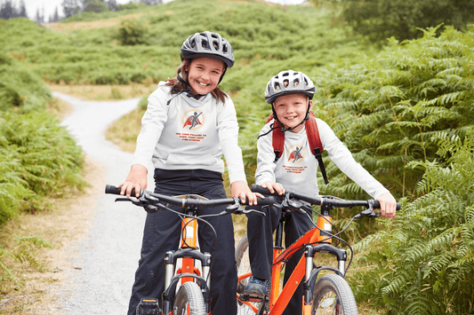 Two children on bicycles, one wearing a helmet, embodying youthful energy and outdoor fun. Use Your Powers Youth Hooded Sweatshirt, 50% cotton, 50% polyester, with kangaroo pocket and twill taping.