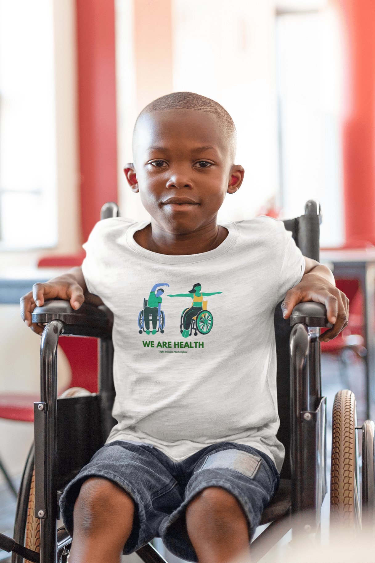 A boy in a wheelchair wearing a white shirt with a wheelchair yoga design. Youth T-shirt made of 100% cotton, durable twill tape shoulders, and curl-resistant collar for everyday comfort.