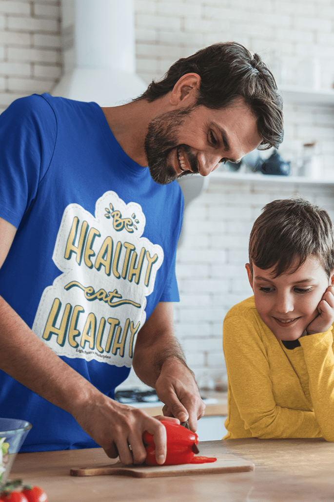 A man and boy cutting vegetables in a kitchen, showcasing the Be Healthy Eat Healthy Unisex T-Shirt. Made from soft 100% ring-spun cotton, featuring twill tape shoulders for durability and a clean crew neckline.